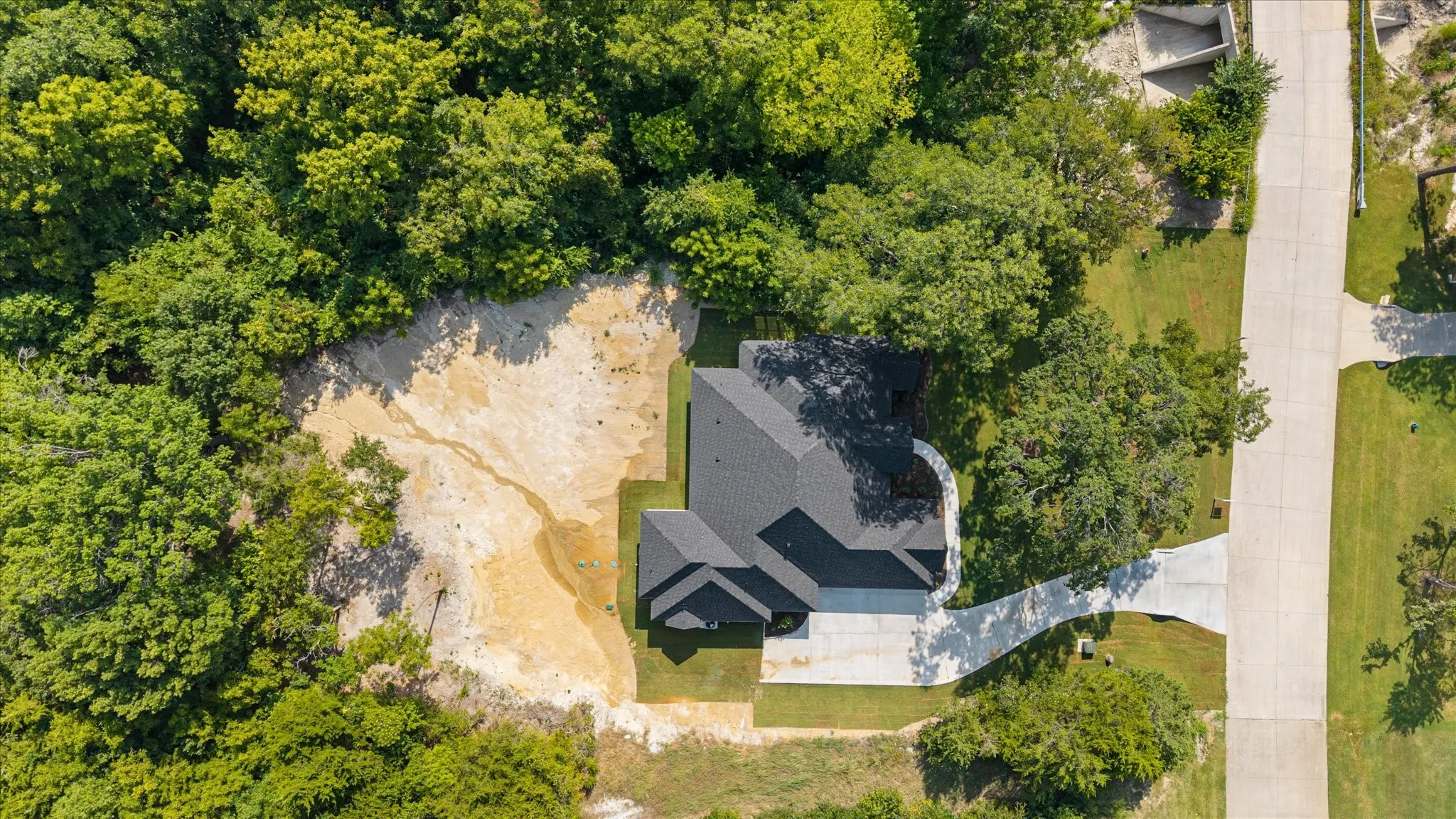 Newly constructed residence with a dark shingle roof, extensive surrounding trees, and a concrete driveway
