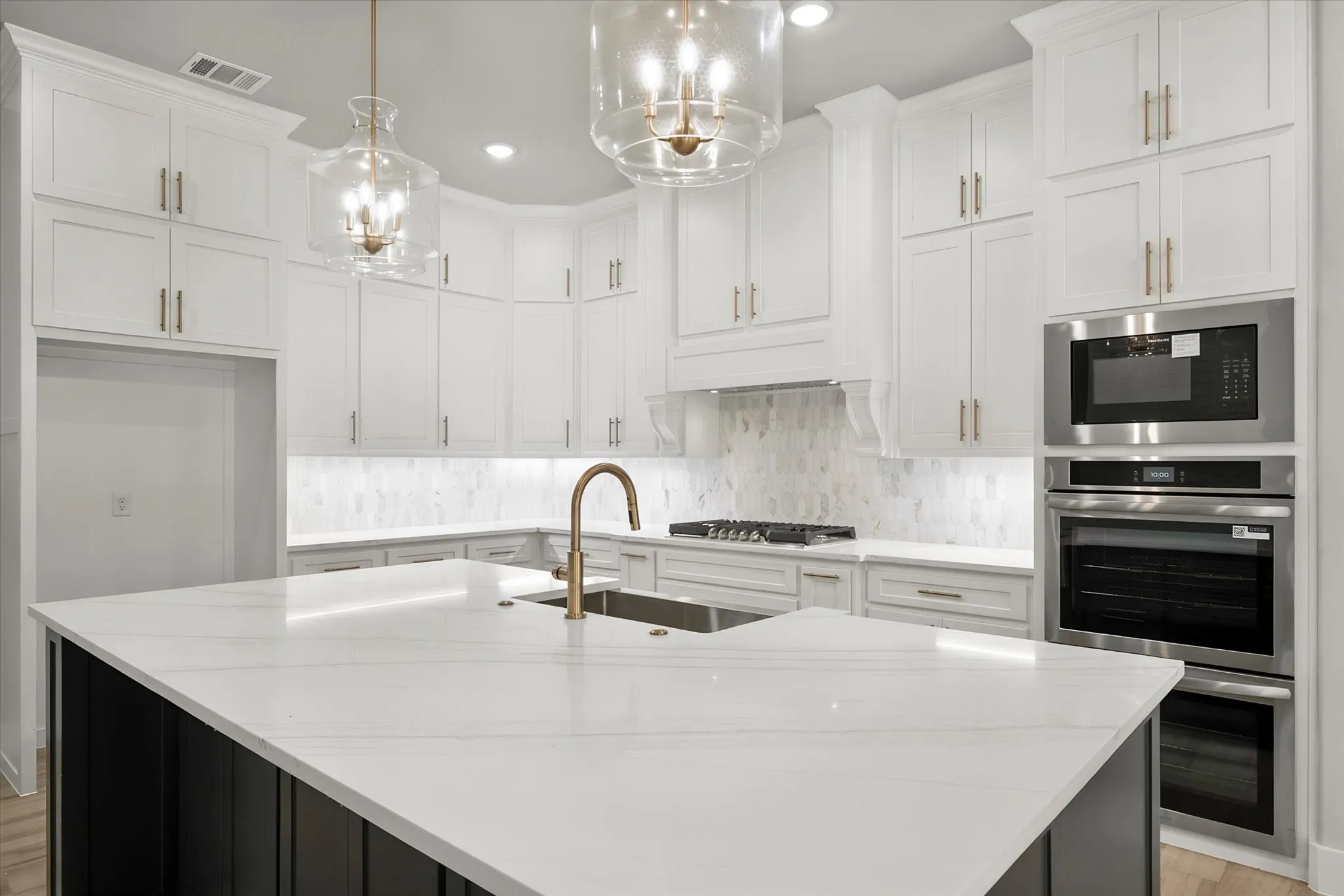 Sophisticated kitchen featuring white shaker-style cabinetry with brushed metal hardware, white subway tile backsplash, and a large waterfall-edge quartz island with seating