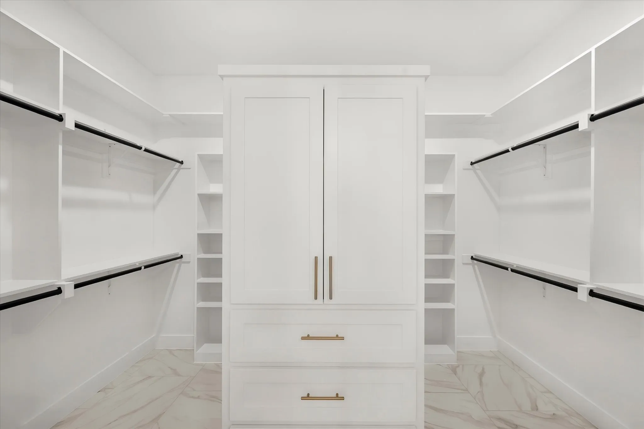 White custom cabinetry with gold hardware, extensive built-in shelving, hanging rods, and large format tile flooring