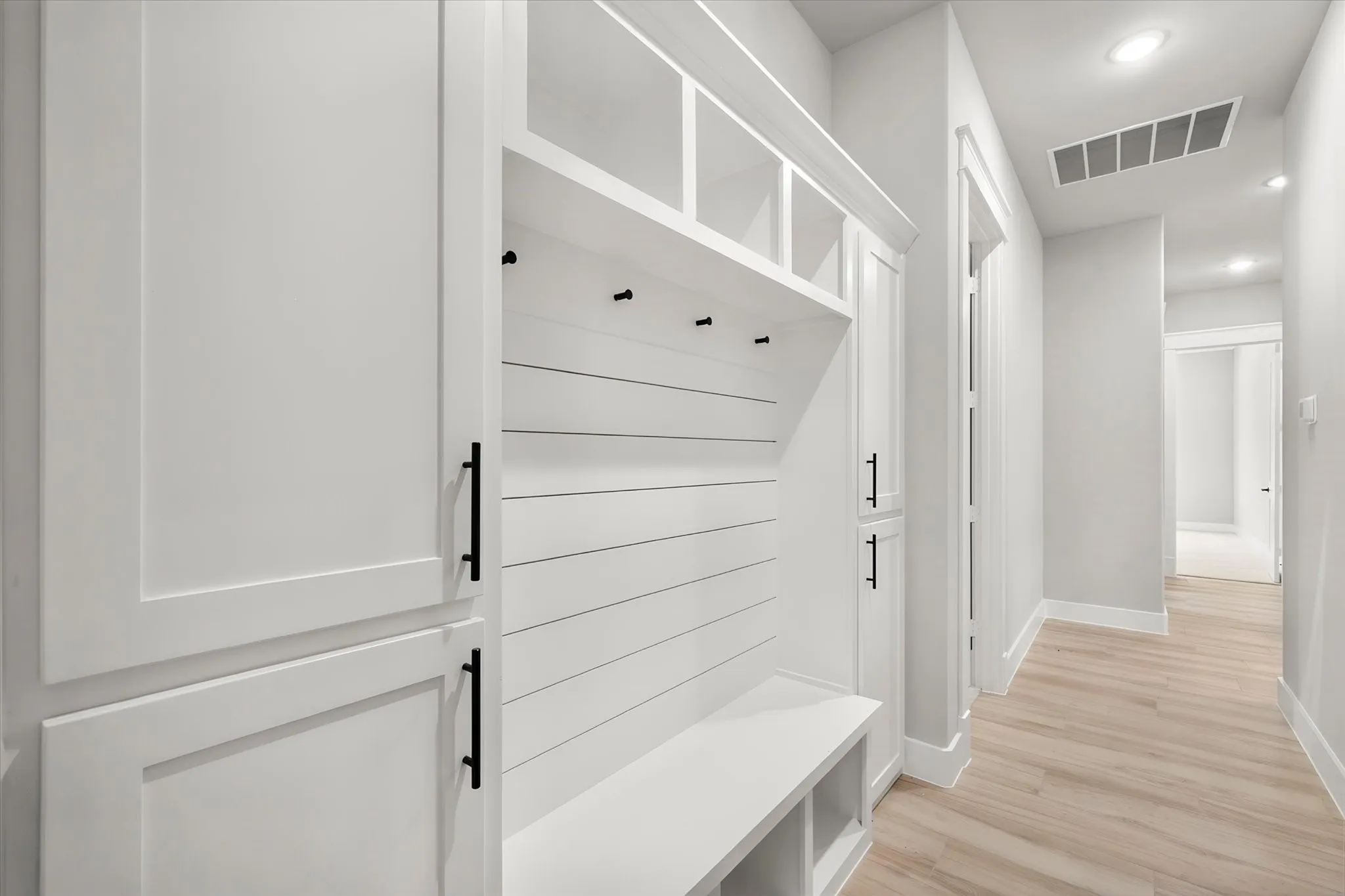 Built-in mudroom bench with cubbies, white shaker cabinetry with black hardware, shiplap detailing, and recessed lighting