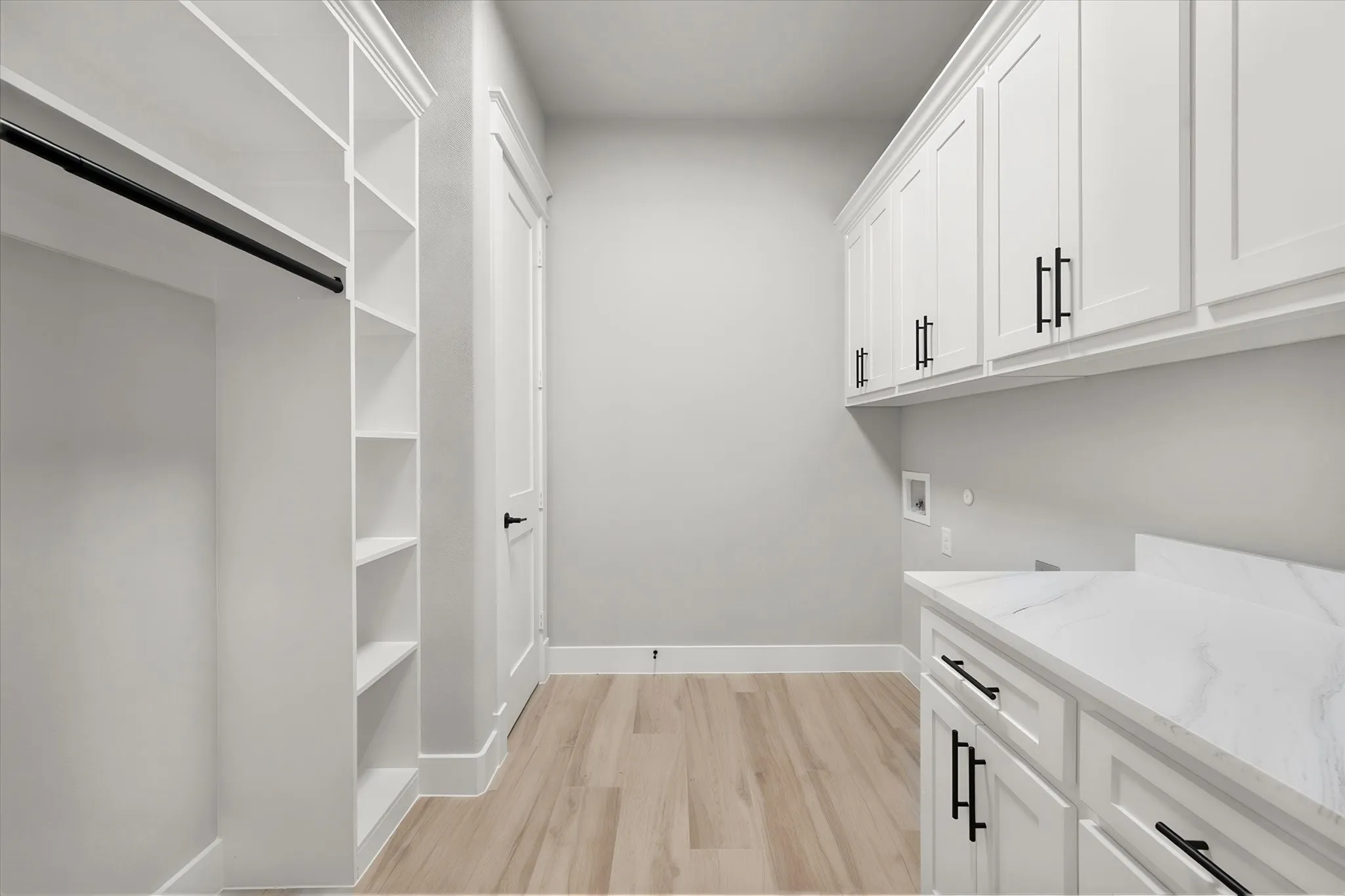 White cabinetry with matte black hardware, wood-finish flooring, built-in shelving, and a patterned countertop