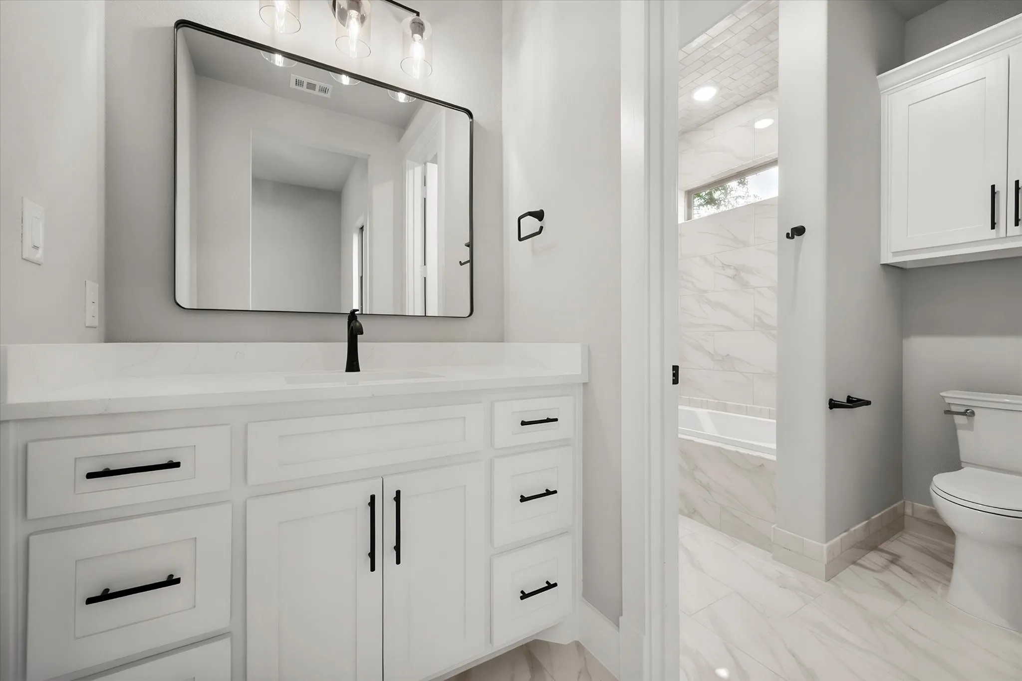 White vanity with a light-colored countertop, rectangular mirror, and matte black fixtures