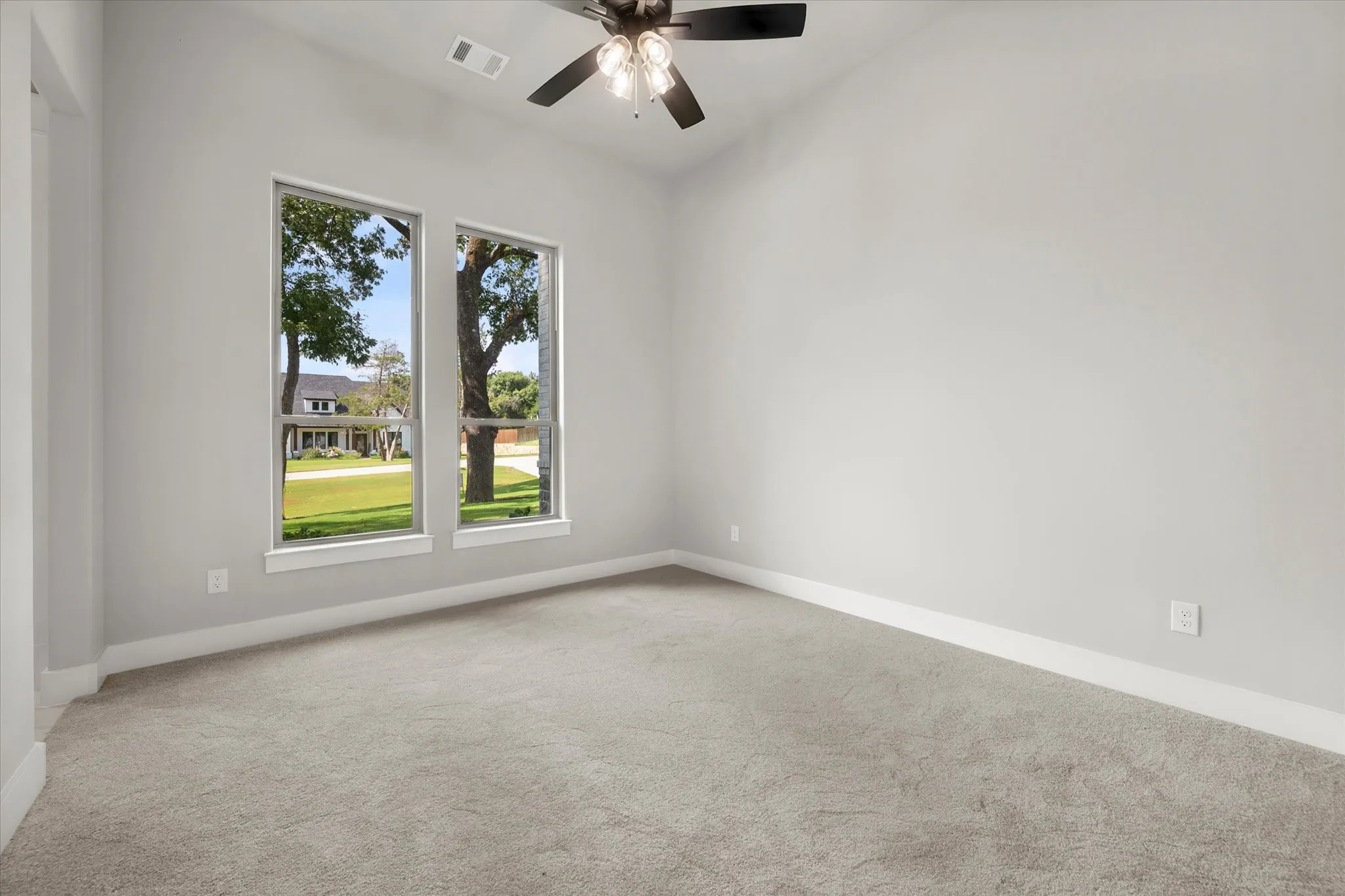 Vaulted ceiling with a ceiling fan, light gray wall paint, two large windows, white trim, and gray carpet flooring