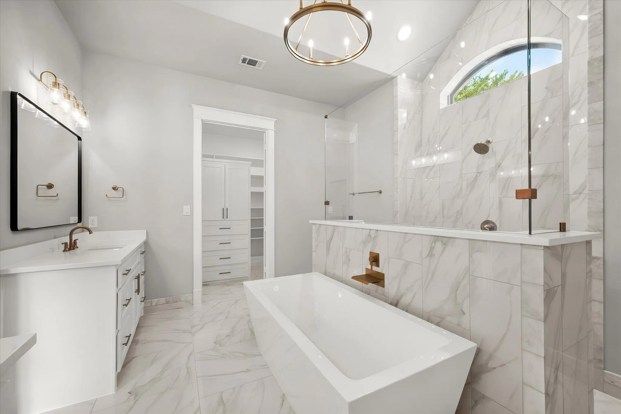 Spacious bathroom featuring a freestanding soaking tub, a walk-in shower with glass enclosure, a white vanity with an undermount sink, and marble-patterned tile flooring and shower surround