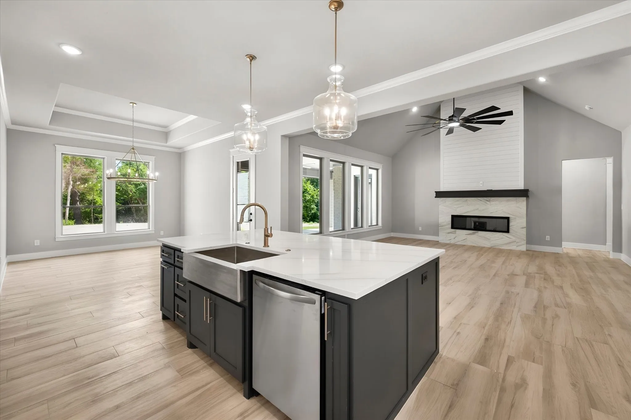Open-concept kitchen and great room featuring a large center island with waterfall-edge countertop, stainless steel appliances, and a farmhouse-style sink