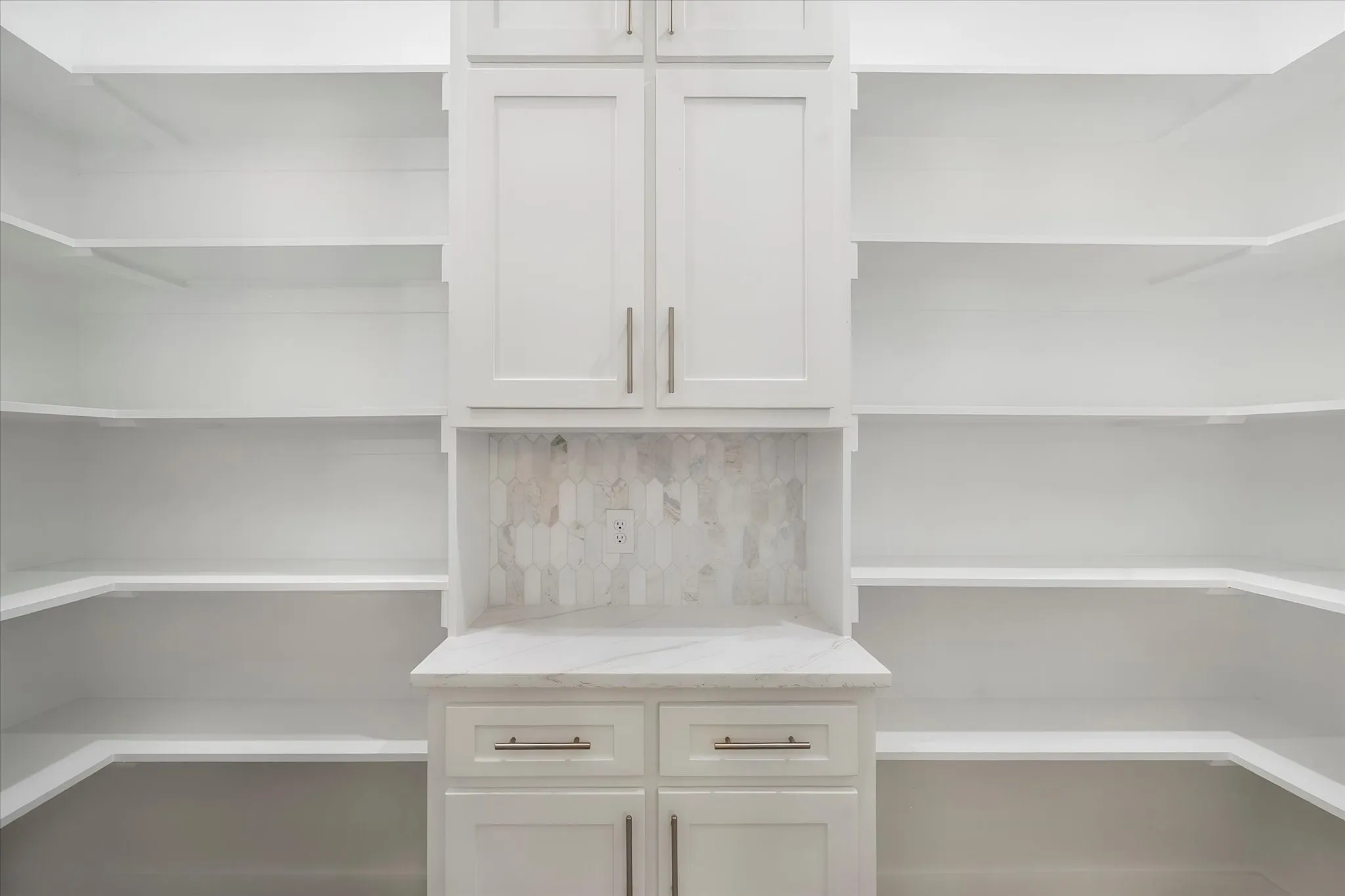 Integrated storage system featuring white shaker-style cabinetry, open shelving, a light-toned backsplash, and a coordinating countertop