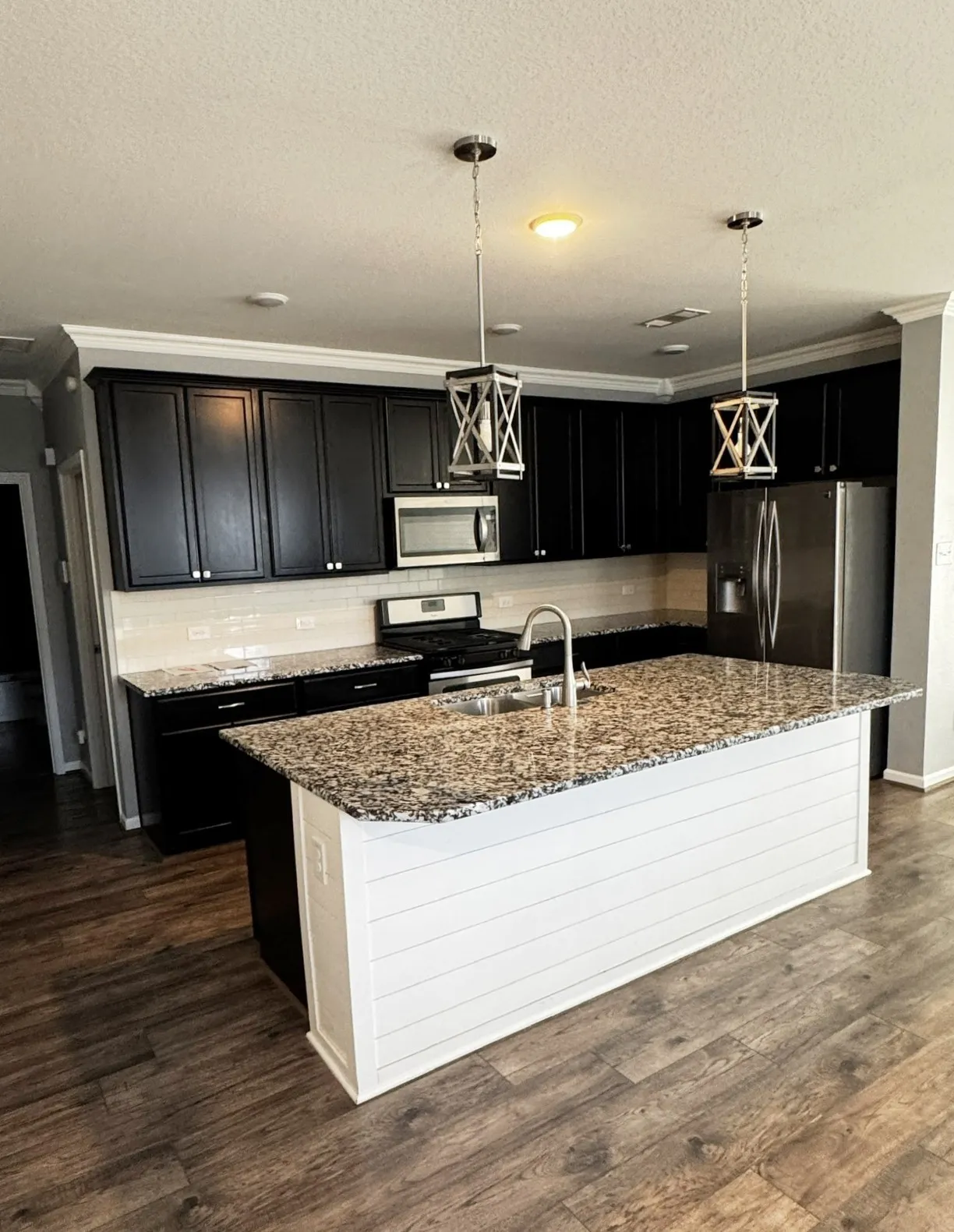 Kitchen featuring wood-finish flooring, dark cabinetry, light-toned countertops, a white shiplap island, and stainless steel appliances