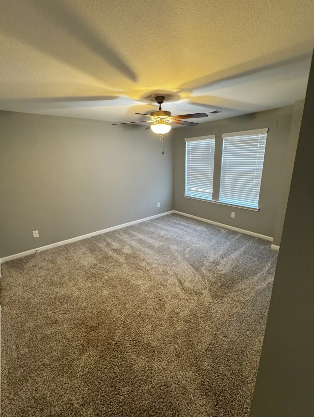 Wall-to-wall carpeting, dual windows with blinds, ceiling fan with integrated lighting, and neutral wall tones
