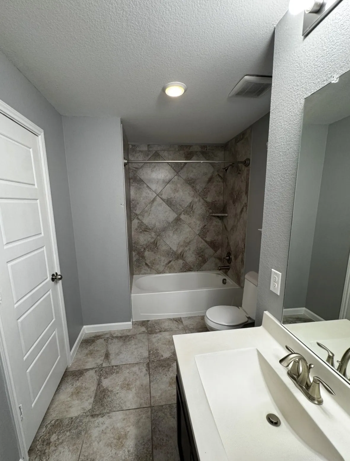Tiled flooring, complete with a bathtub and shower featuring tiled surround, a toilet, a vanity with an integrated sink, and an overhead vanity light