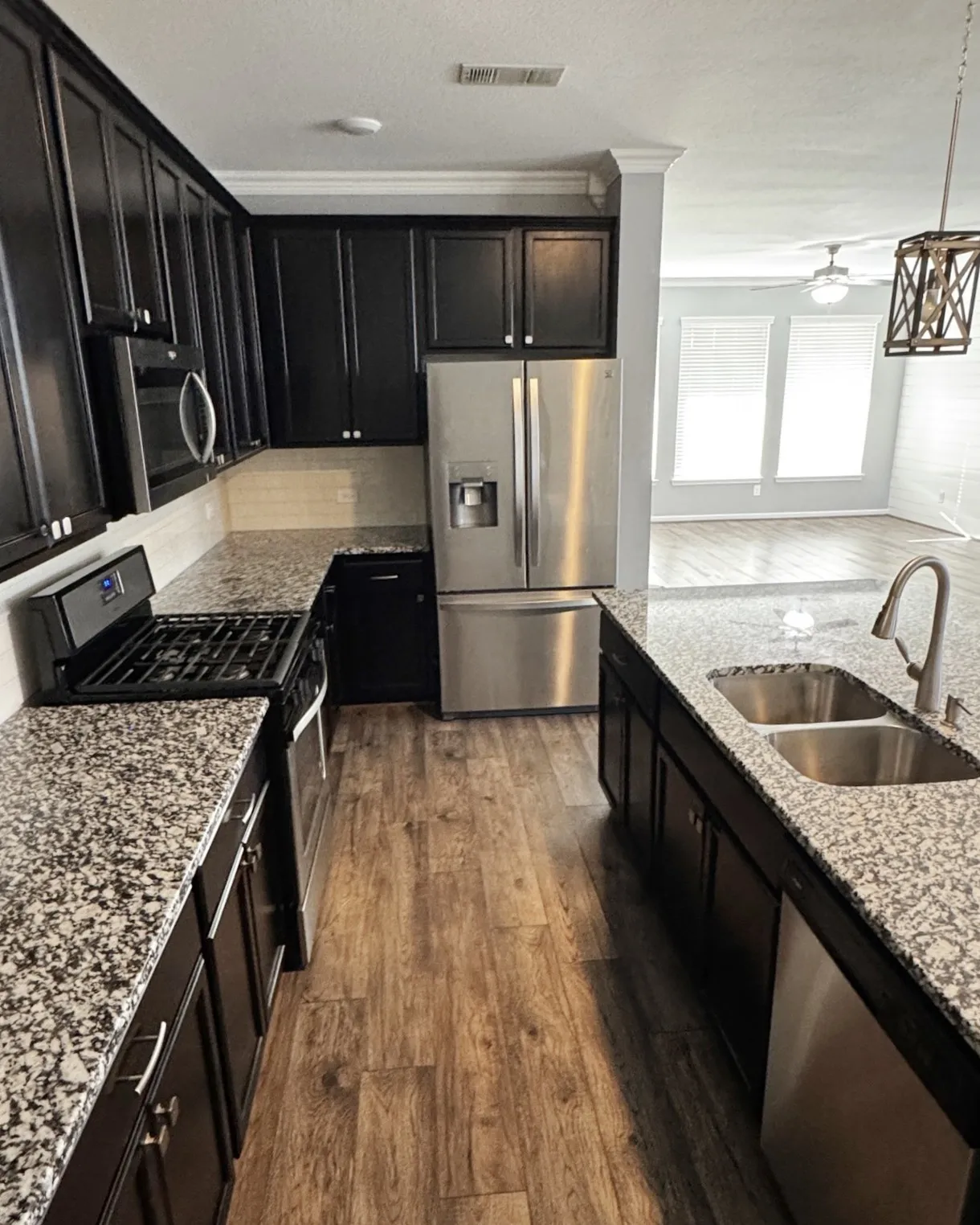 Kitchen featuring dark wood-finish cabinetry, light-toned backsplash, stainless steel appliances, speckled stone countertops, and wood-finish flooring