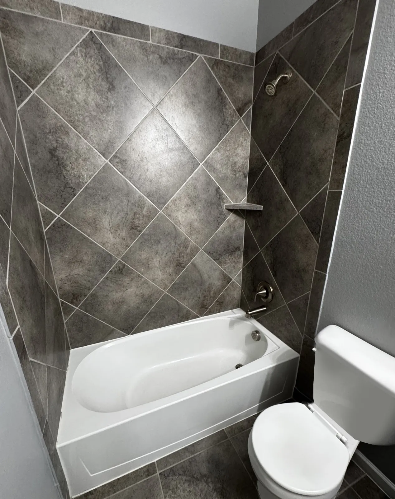 Bathroom featuring a built-in bathtub, a shower with a built-in shelf, and diagonal dark-toned wall tiling