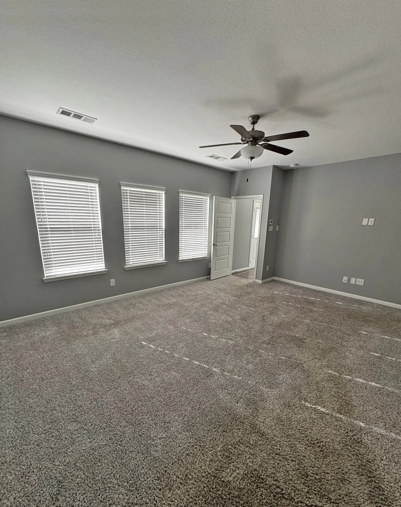 Spacious room featuring neutral carpeting, a ceiling fan with integrated lighting, multiple windows with blinds, and light-colored walls