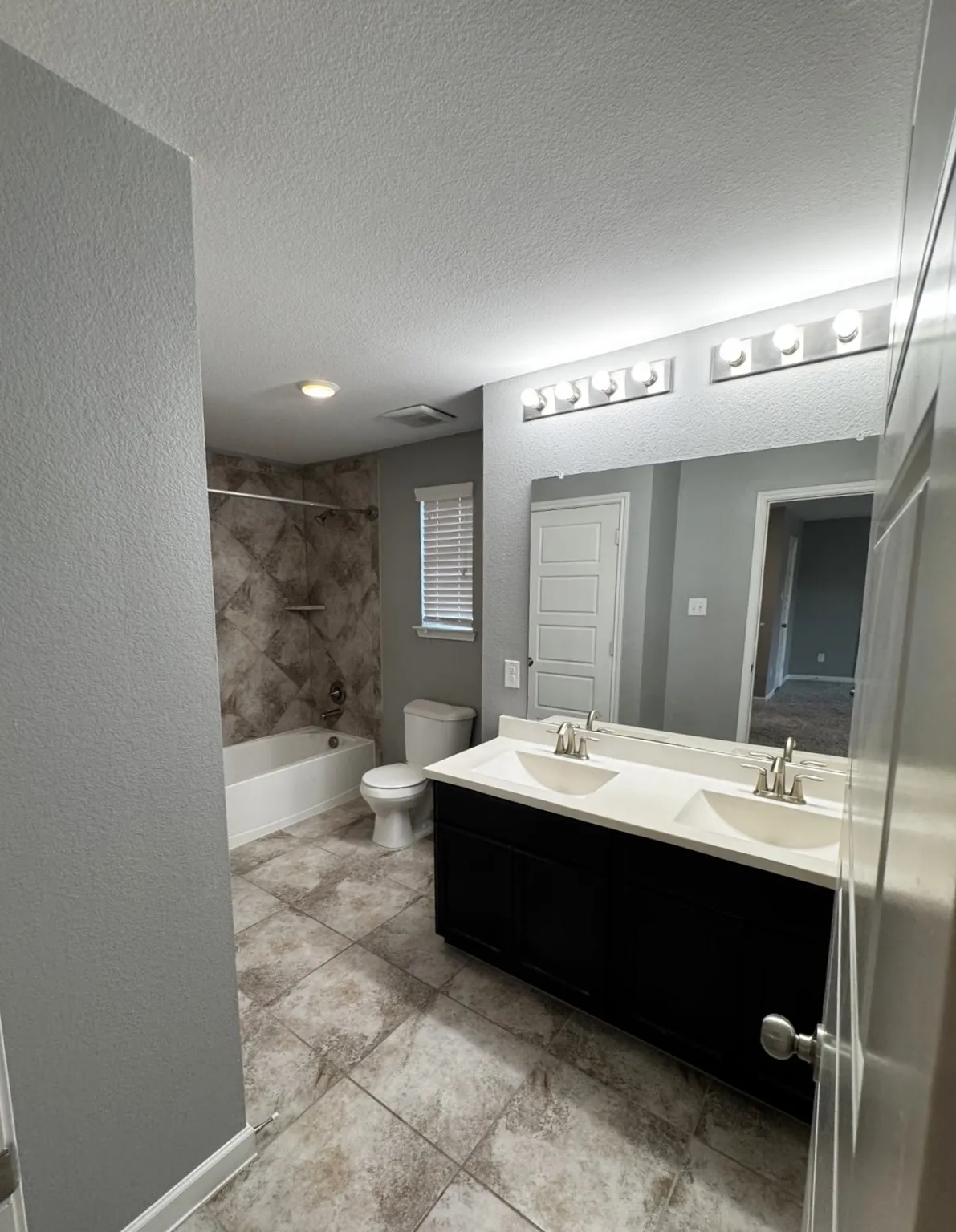 Double vanity with white solid surface countertops, a full-width mirror, and two contemporary light fixtures