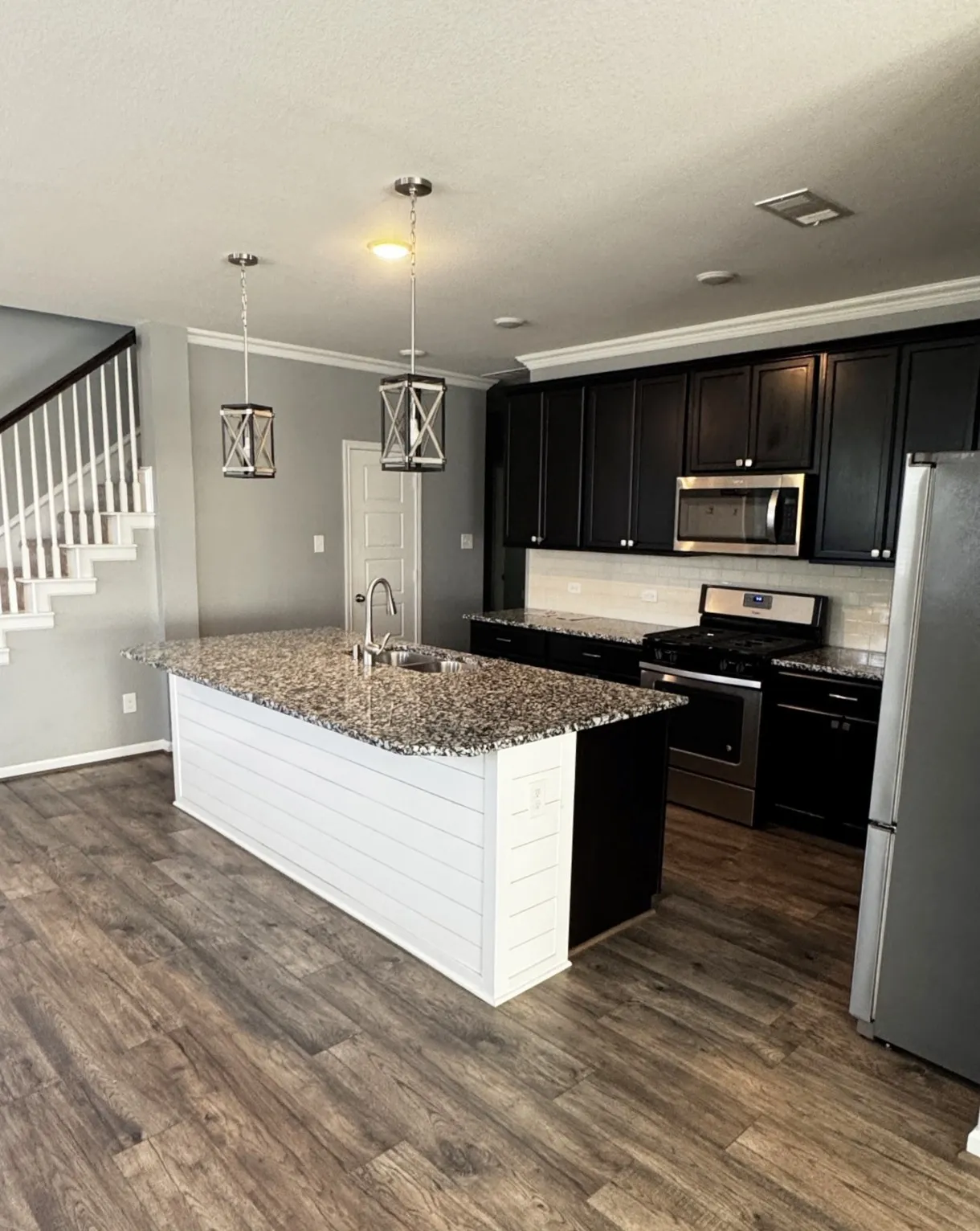 Kitchen featuring a center island with a granite countertop and integrated sink, dark wood-finish cabinetry, stainless steel appliances, and wood-finish flooring
