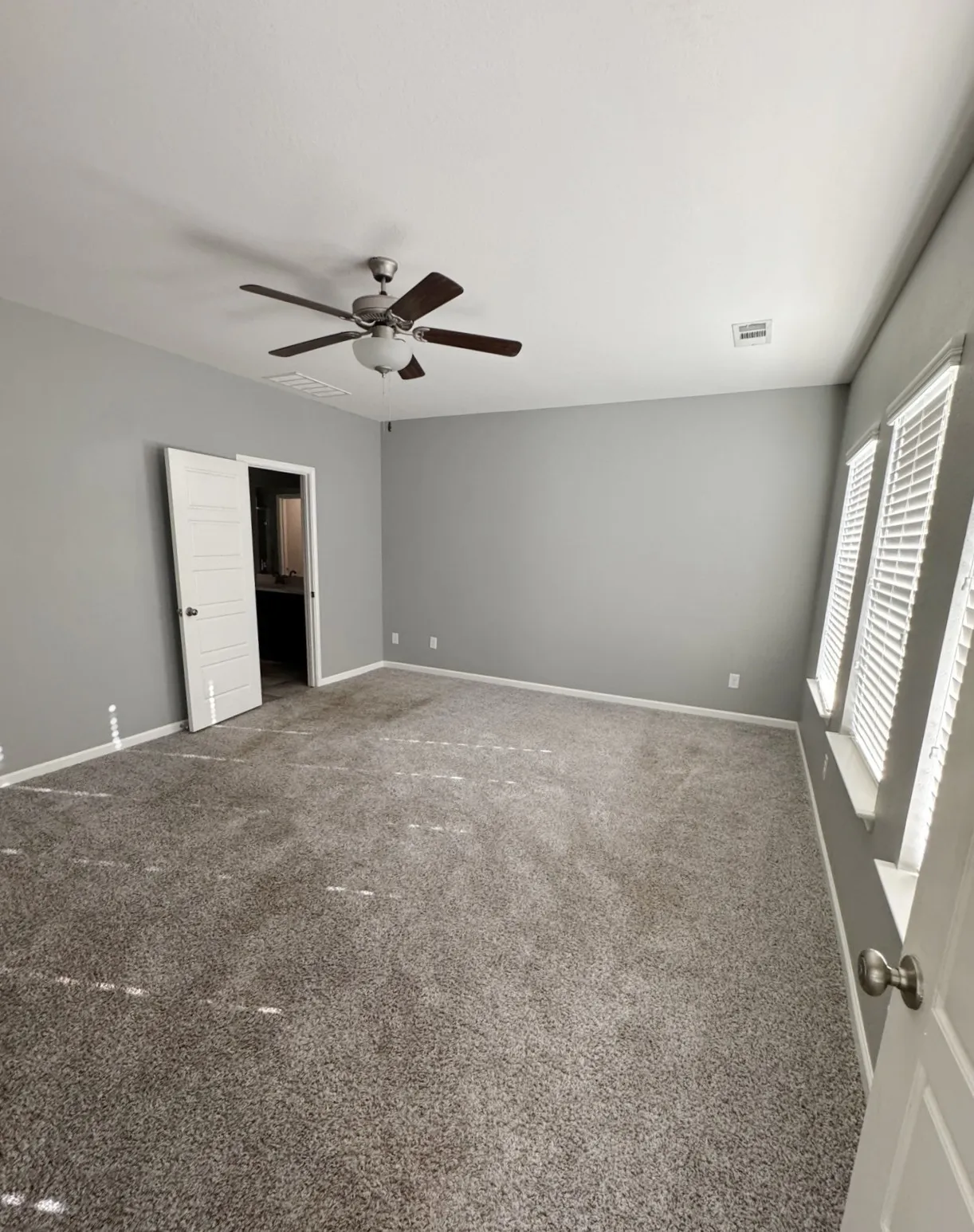 Spacious room featuring gray carpet flooring, multiple windows with blinds, a ceiling fan with integrated lighting, and neutral wall tones