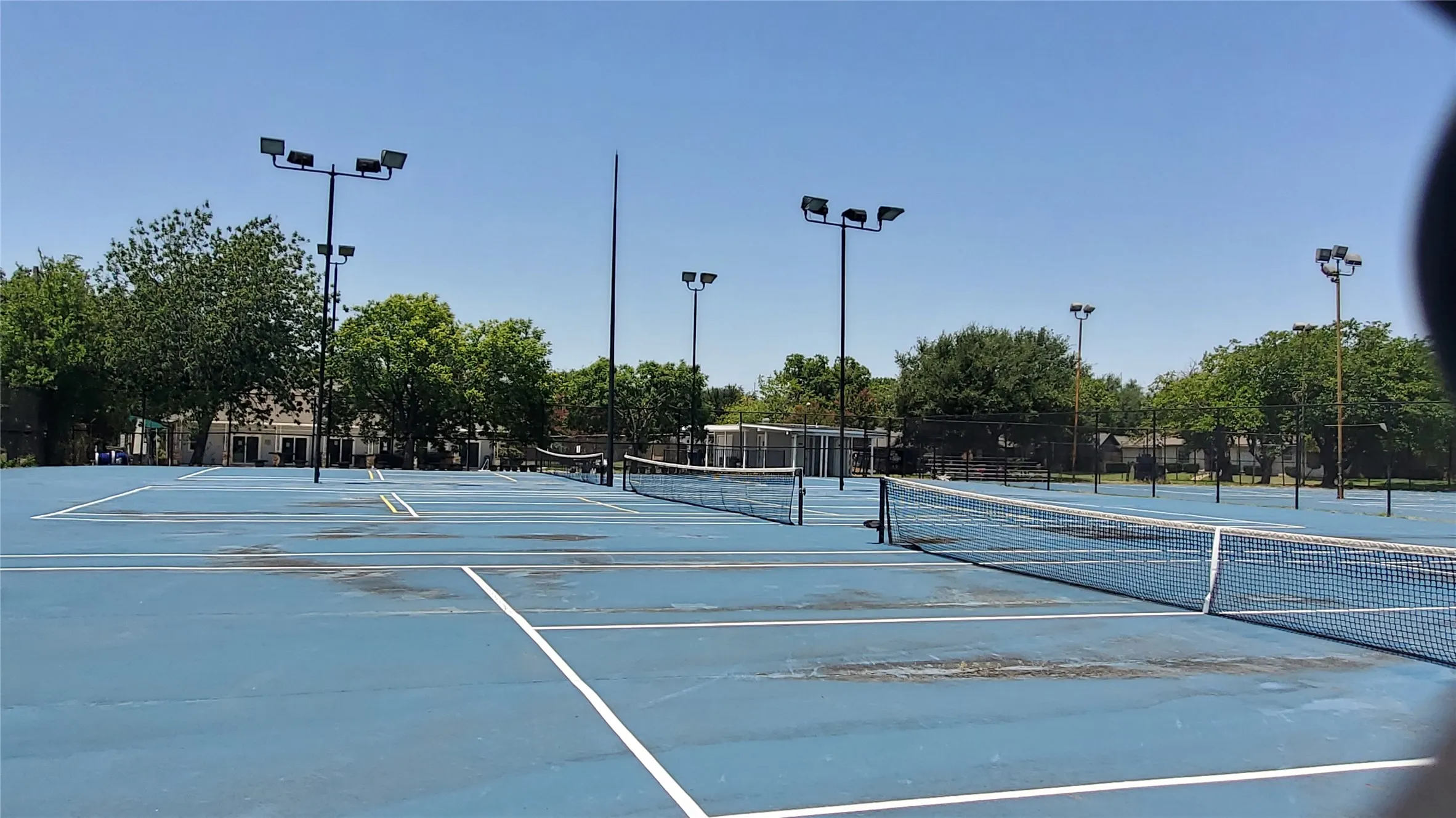 Multiple outdoor tennis courts with blue surfacing and white line markings