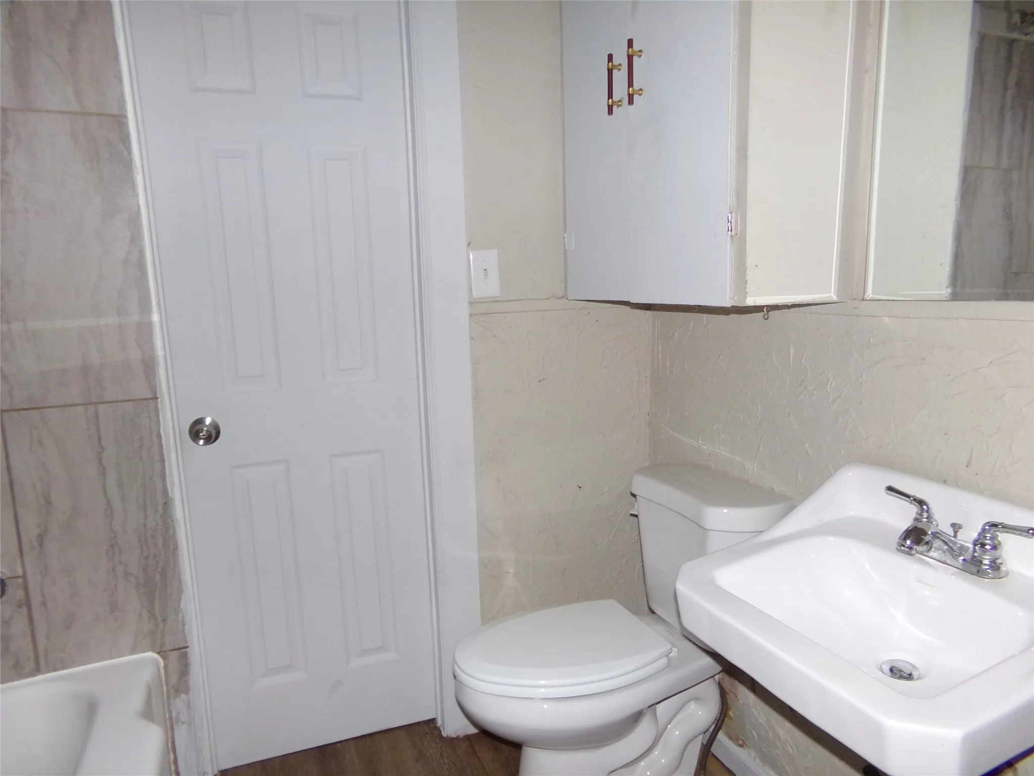 Bathroom with a pedestal sink featuring chrome hardware, white toilet, and wood-finish flooring