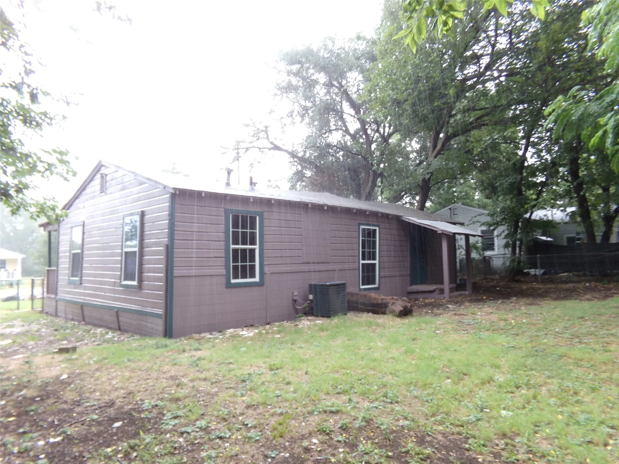 Single-story residence featuring brown horizontal siding with green trim, white window frames, and a covered porch area
