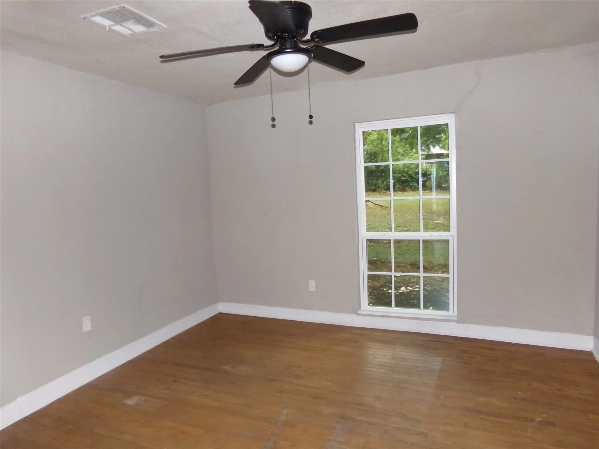 Interior space featuring wood-finish flooring, light neutral wall tones, a ceiling fan with integrated lighting, and a multi-pane window