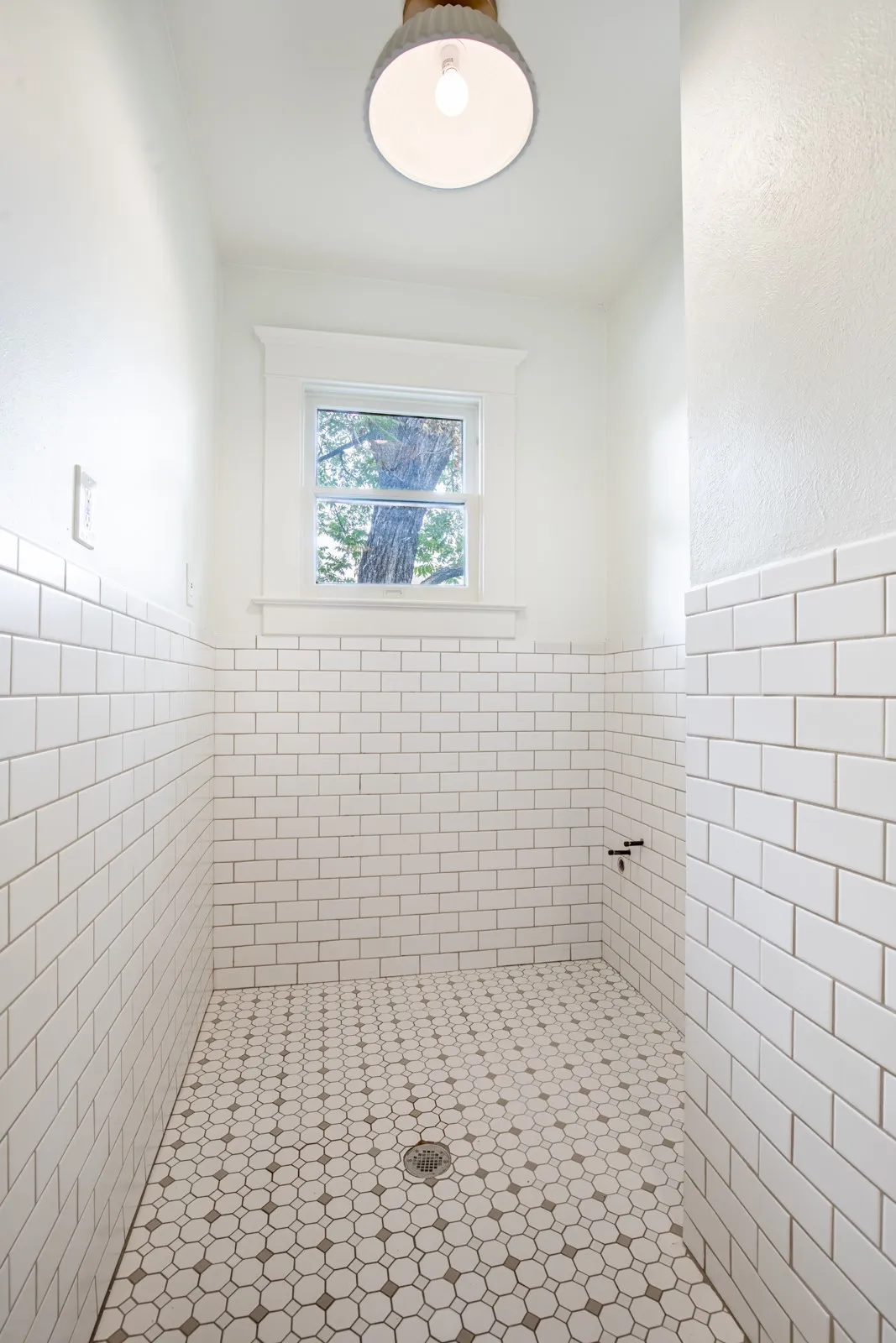 Shower enclosure featuring white subway tile walls, patterned mosaic tile flooring, and a single window