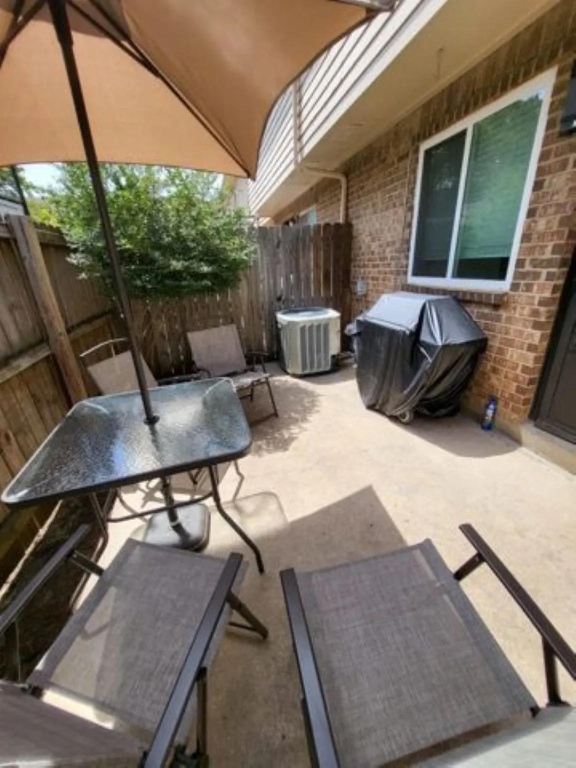 Paved patio area featuring a brick exterior wall, a large window, and a wood privacy fence