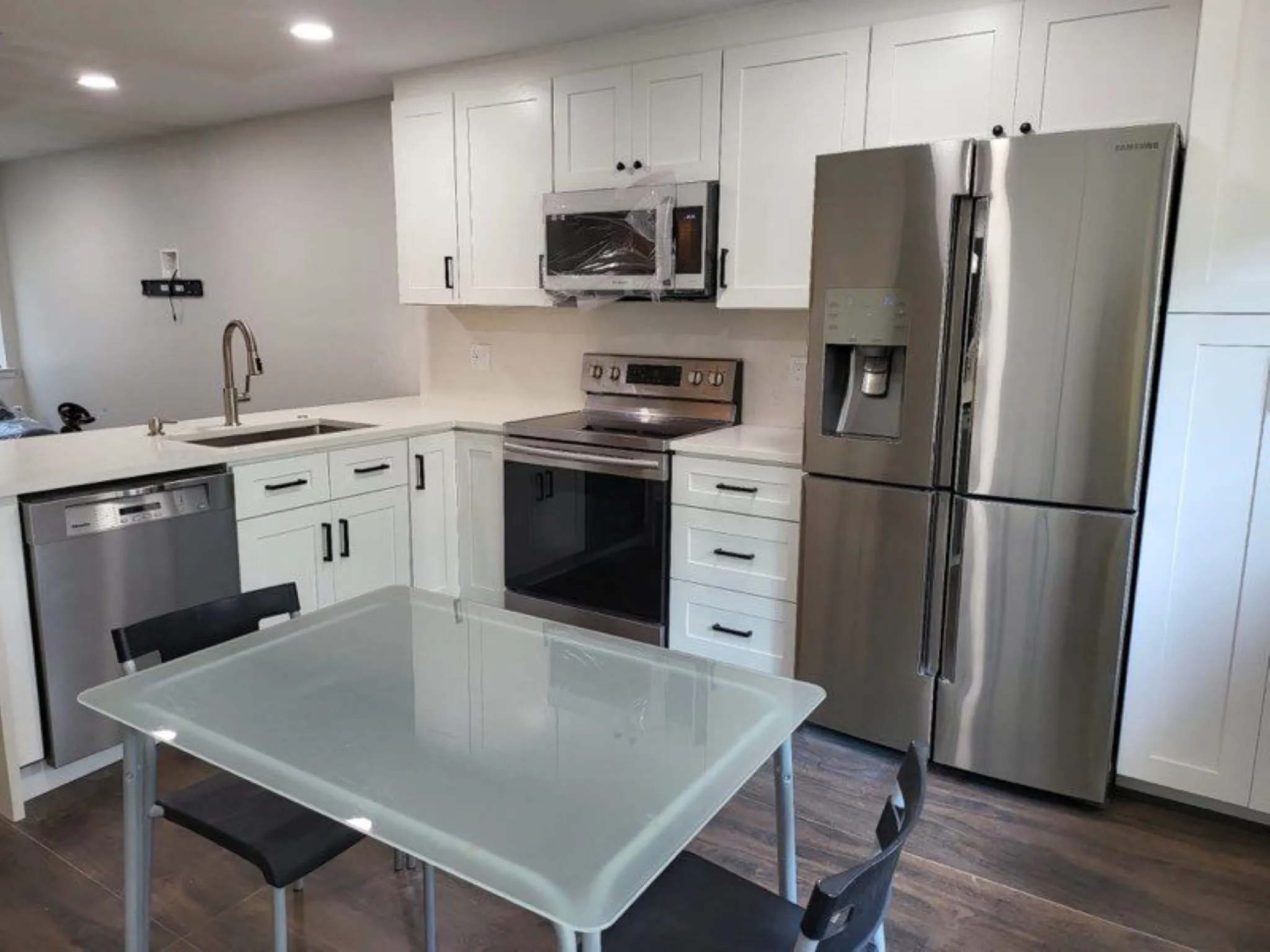 Contemporary kitchen featuring white shaker-style cabinetry, stainless steel appliances, white countertops, and wood-finish flooring