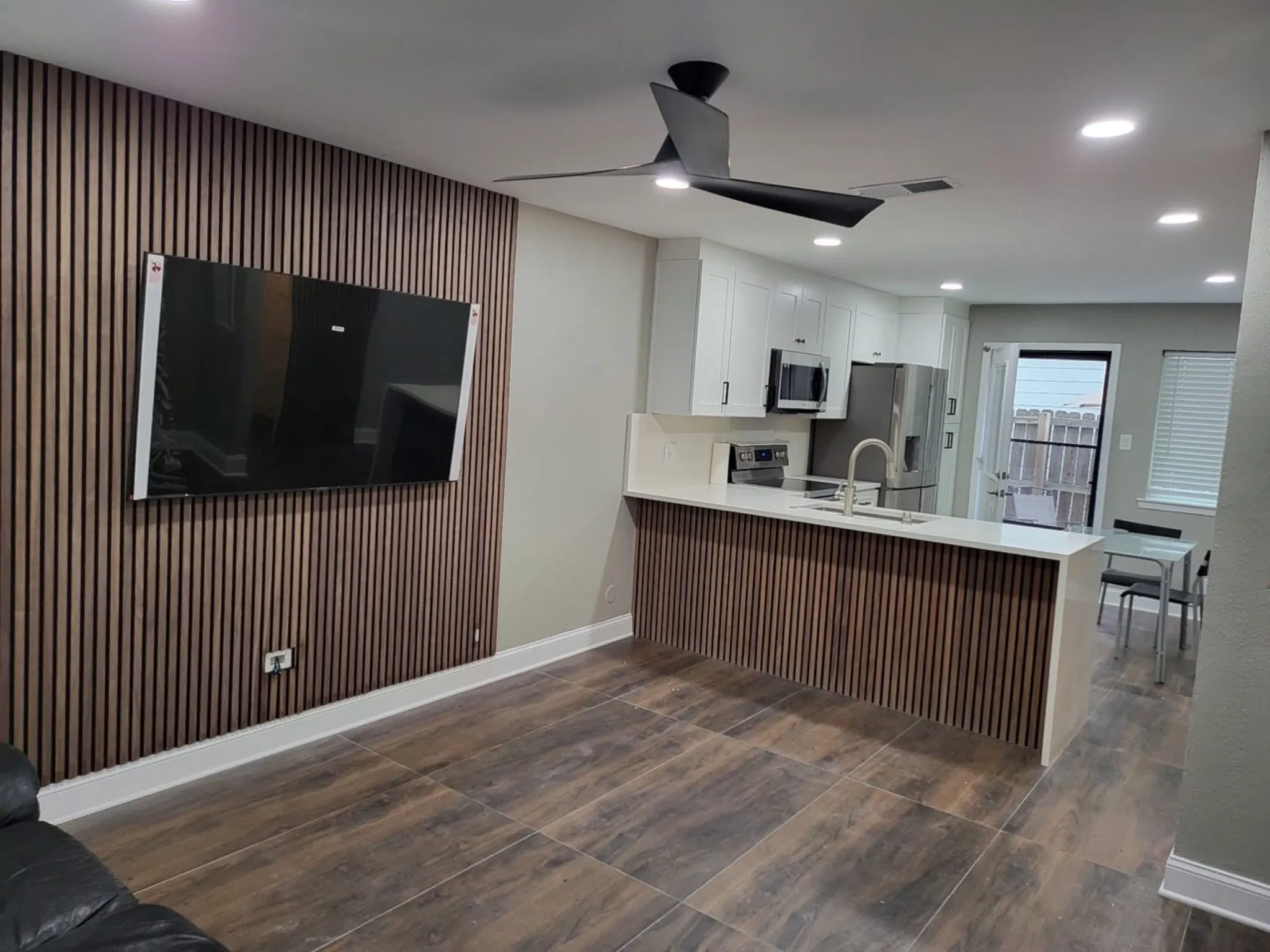Open-concept living area featuring wood-finish accent wall, contemporary ceiling fan, and large format tile flooring