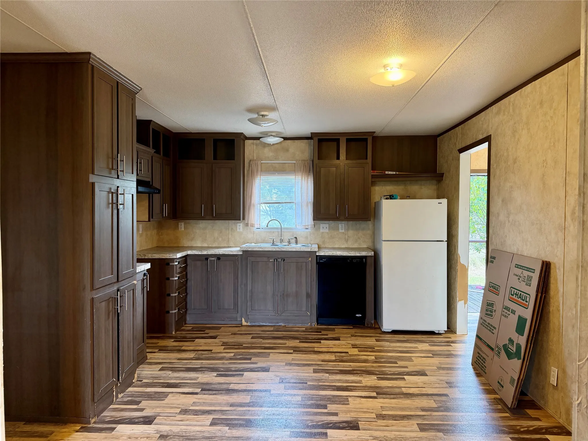 Kitchen featuring wood-finish flooring, dark wood cabinetry, light countertops, and a stainless steel sink with a gooseneck faucet