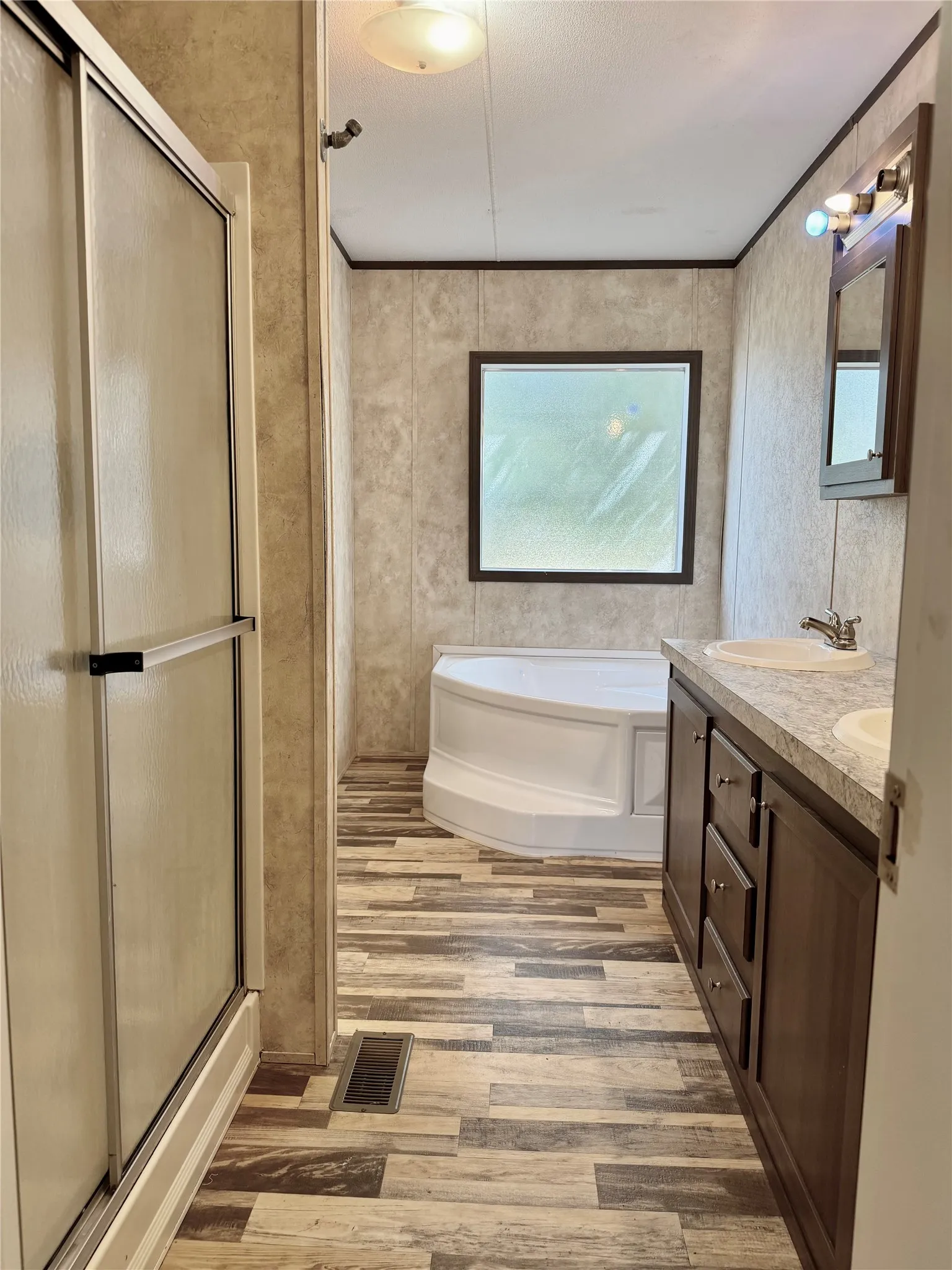 Full bathroom featuring a shower with sliding glass doors, a corner soaking tub, a double vanity with integrated sinks, wood-finish cabinetry, and wood-finish flooring