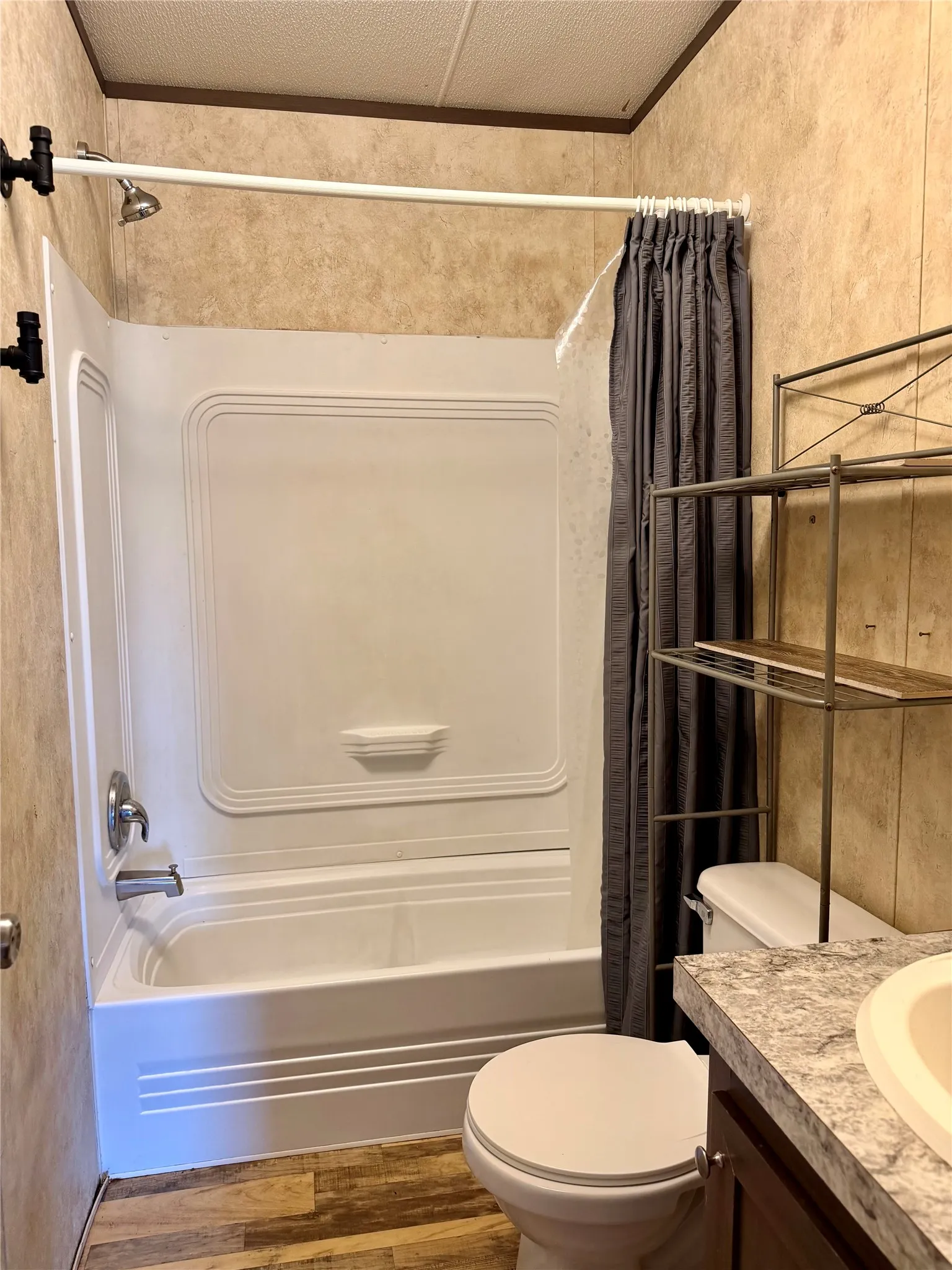Bathroom featuring a white bathtub and shower combination with a curved shower curtain rod, a white toilet, and wood-finish flooring