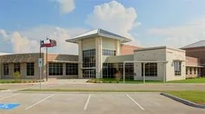 Modern institutional building featuring a prominent central entrance with expansive windows, a distinctive multi-tiered roofline, and light-toned exterior masonry