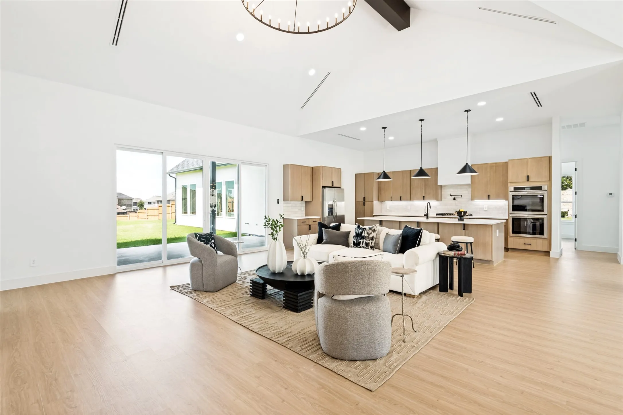 Open-concept living space featuring vaulted ceilings, light wood-finish flooring, and a modern kitchen with a large island and stainless steel appliances