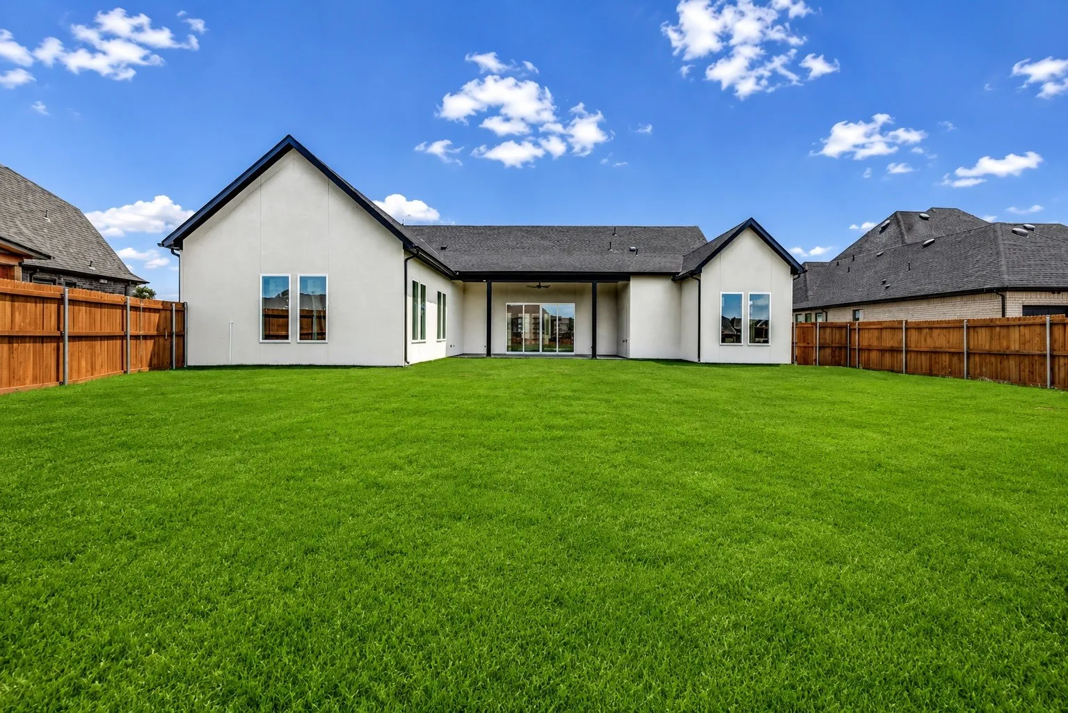 Spacious backyard featuring a lush green lawn, full wood privacy fencing, and a covered patio with sliding glass doors