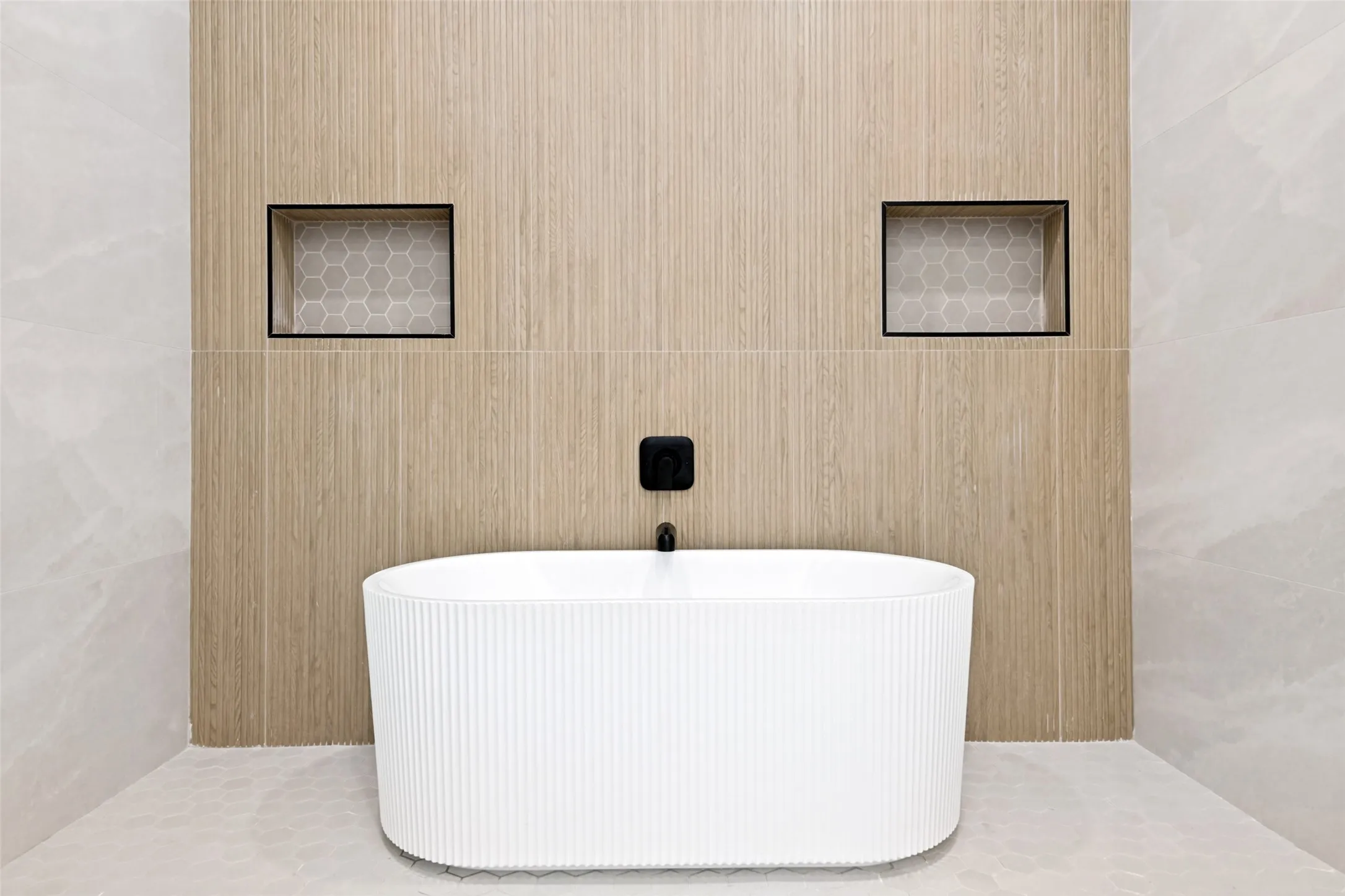 Freestanding fluted bathtub set against a wood-look tile feature wall