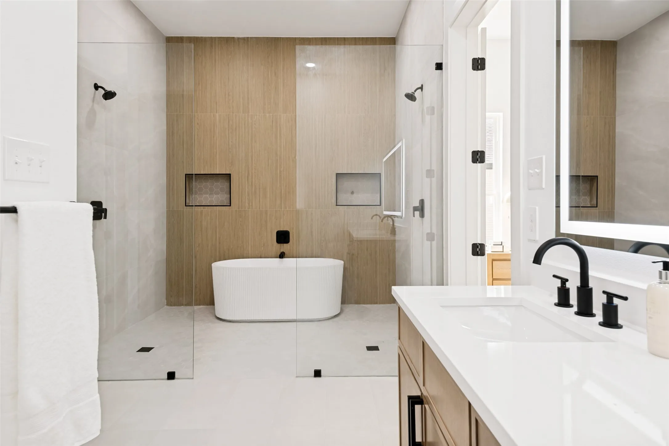 Contemporary bathroom featuring a freestanding tub, glass-enclosed shower, wood-finish accent wall, built-in shelving, and a vanity with an integrated sink