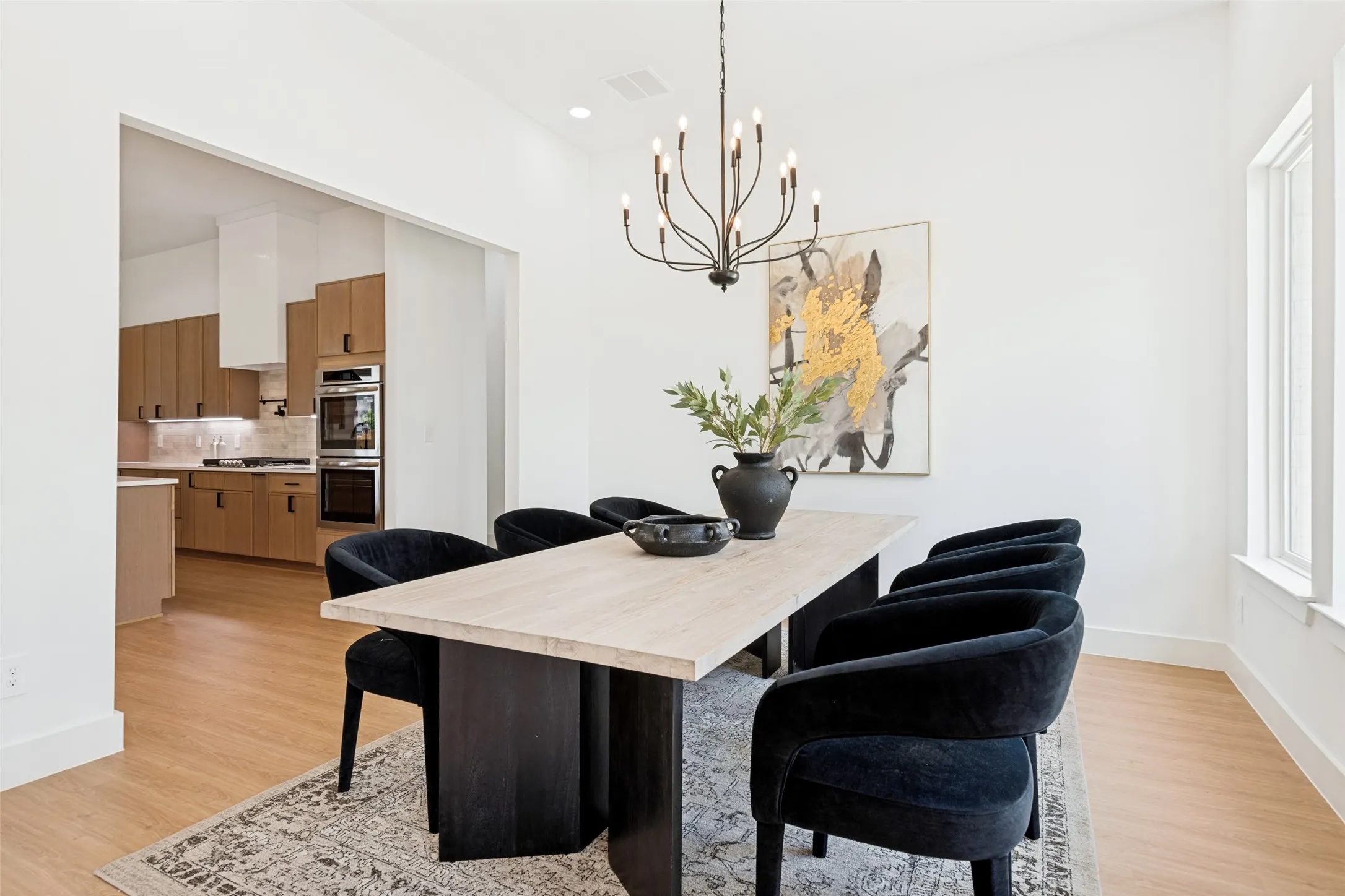 Open-concept dining area featuring light wood-finish flooring, a contemporary black metal chandelier, and recessed lighting