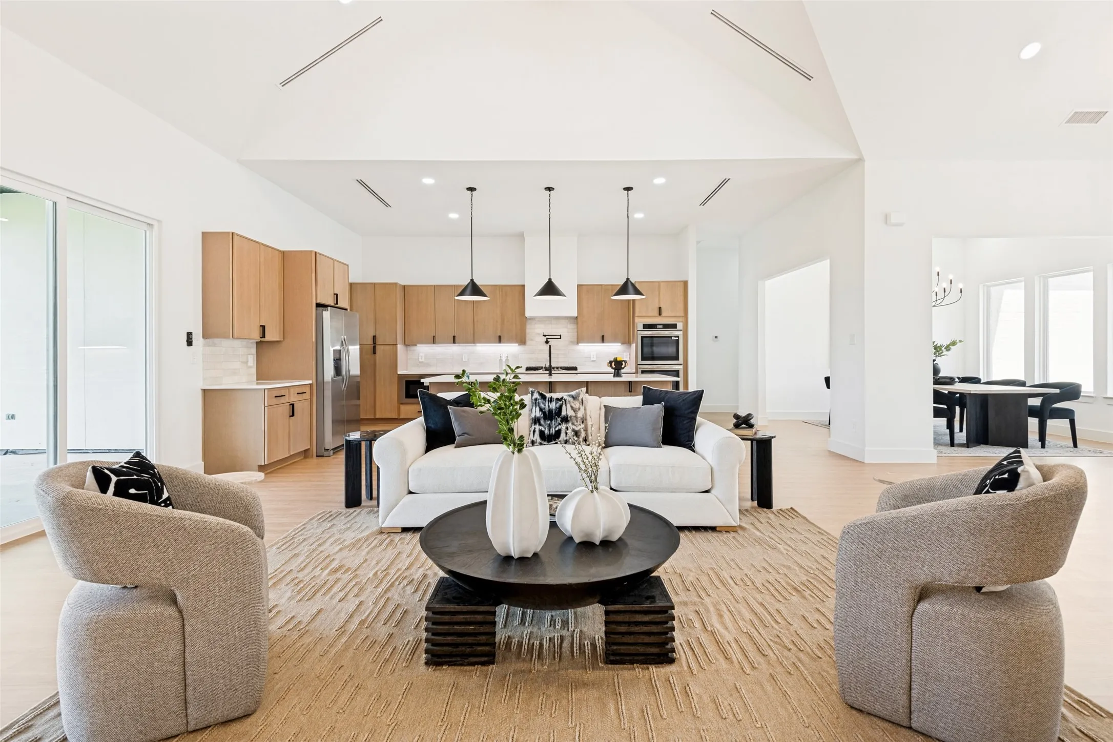 Spacious living area featuring high vaulted ceilings, light wood-finish flooring, and a kitchen with light wood cabinetry