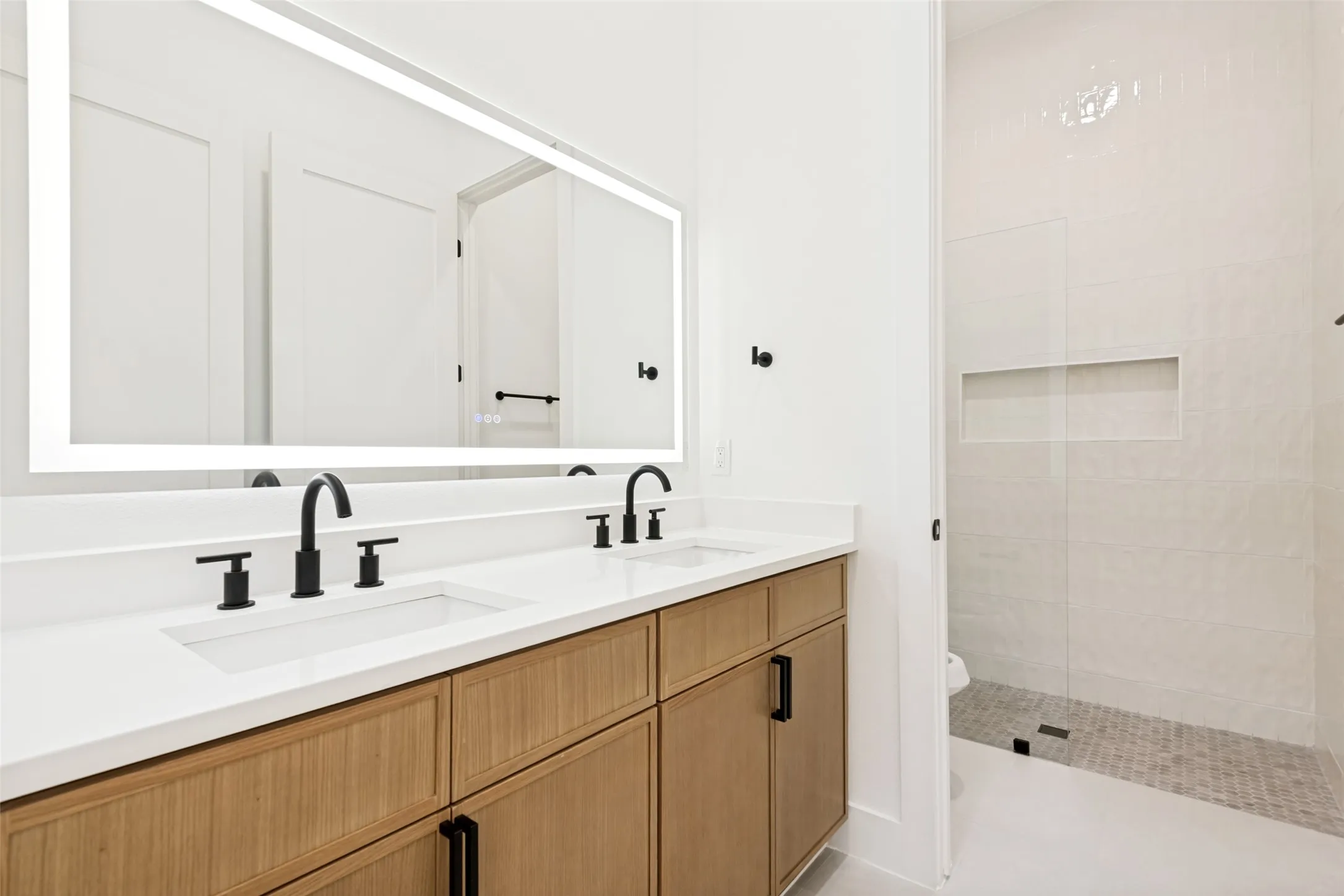 Double vanity featuring wood-finish cabinetry, white countertops, and matte black fixtures