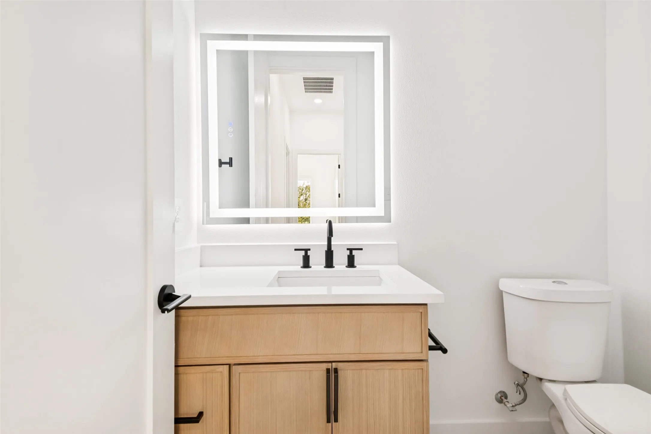 Bathroom featuring a light wood vanity with a white countertop, undermount sink, and matte black faucet