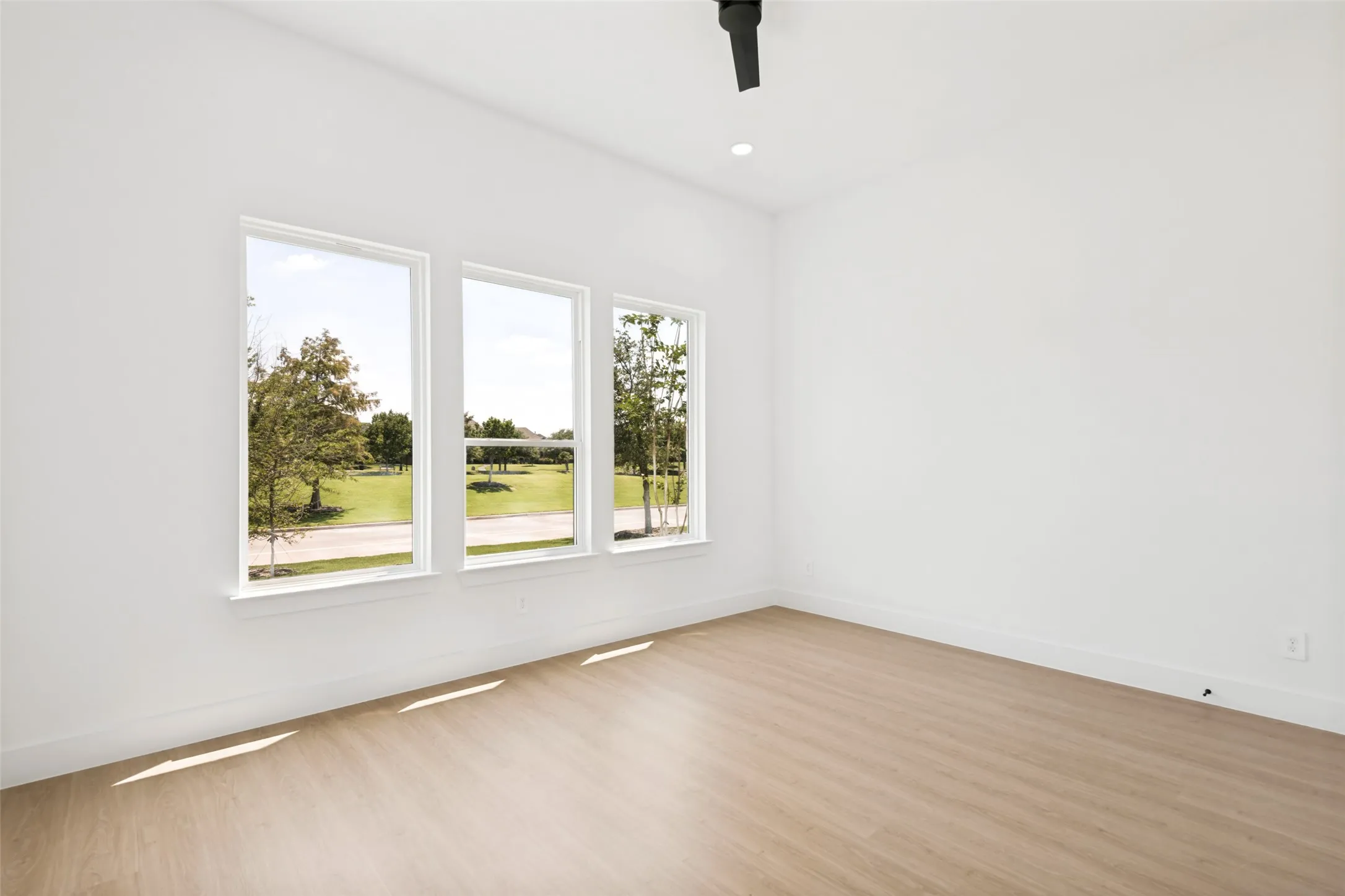 Room featuring three large windows, light wood-finish flooring, white walls, and a contemporary ceiling fan