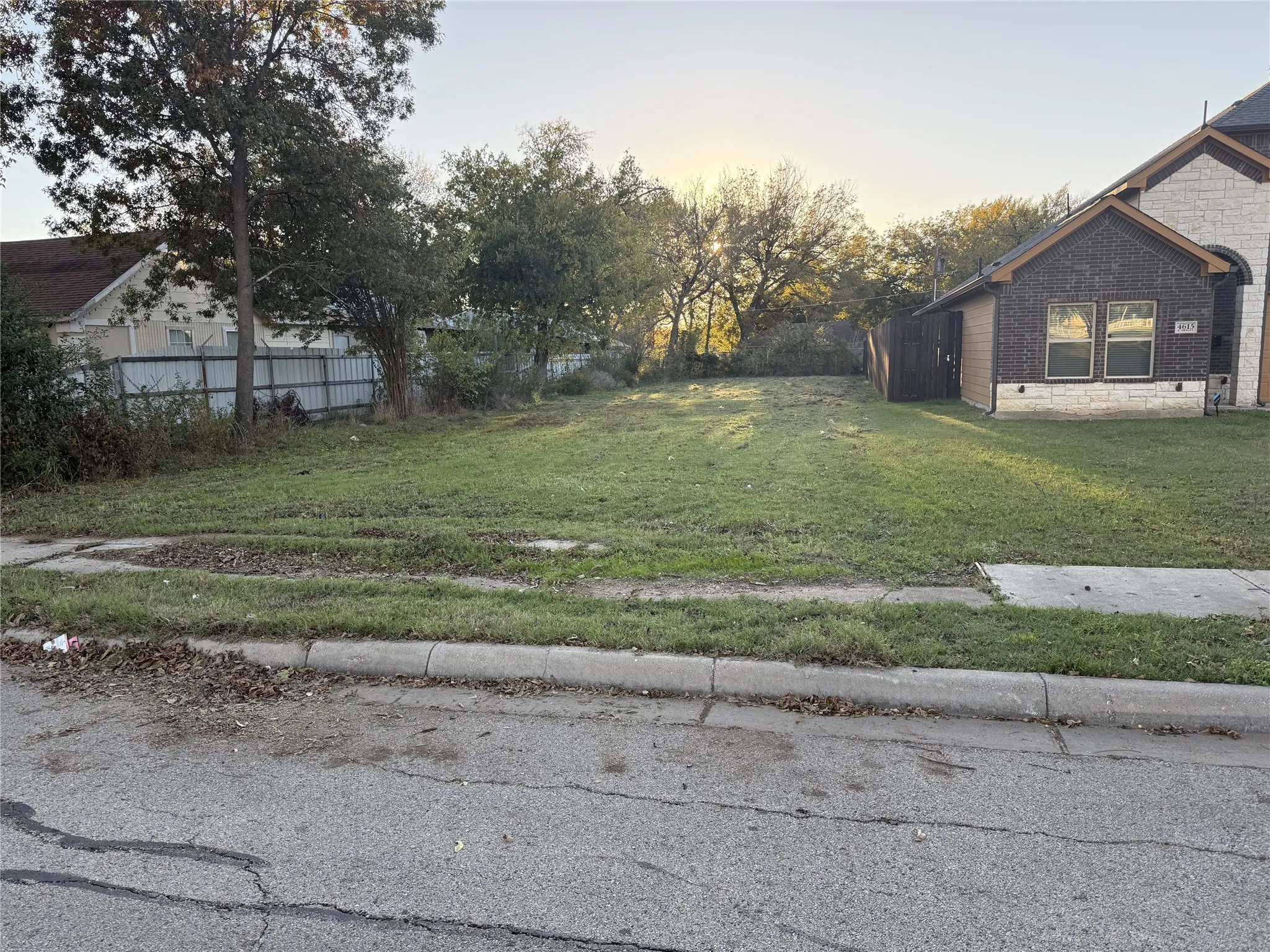 Expansive level lot featuring mature perimeter trees, a concrete sidewalk, and curb access