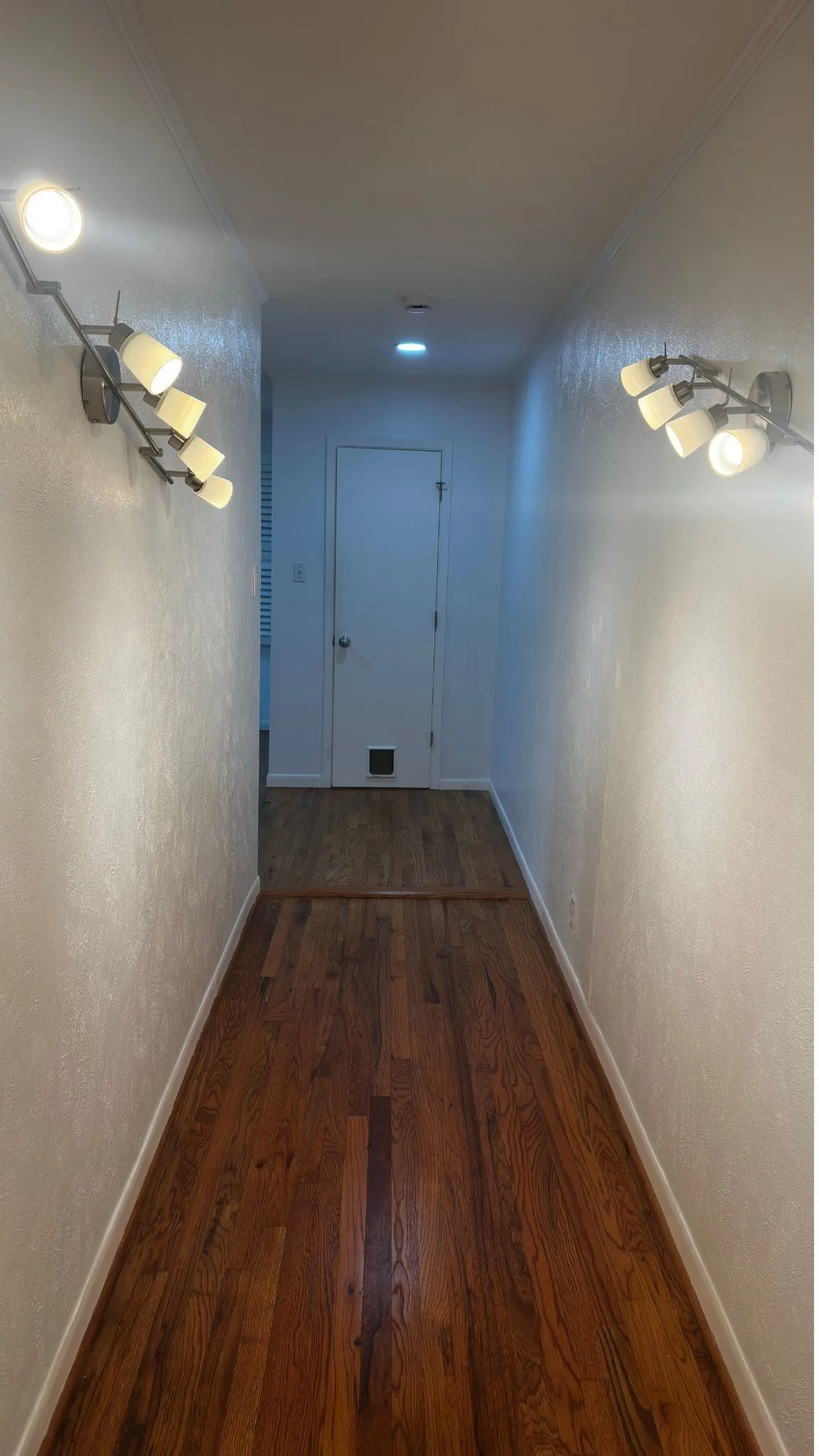 Hallway featuring wood-finish flooring, textured walls, and decorative wall sconces
