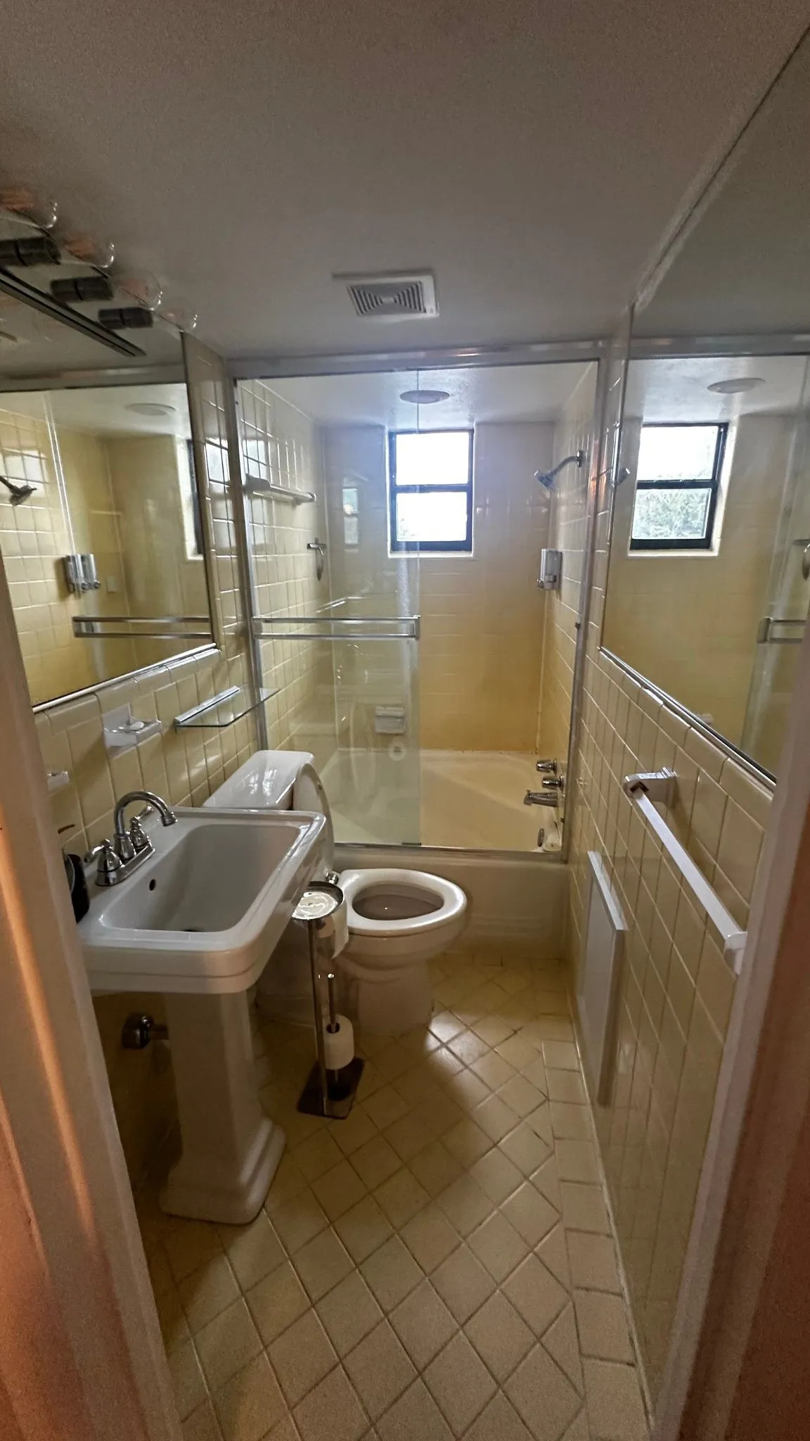 Bathroom featuring a pedestal sink with chrome fixtures, a toilet, and a bathtub with a clear glass enclosure