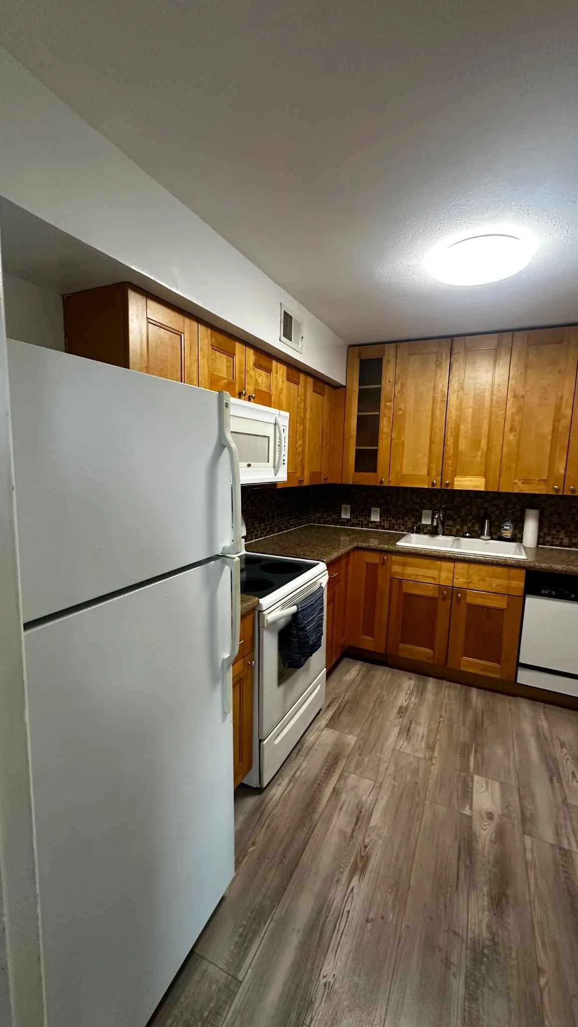 Kitchen featuring wood-finish flooring, white appliances, and warm-toned cabinetry