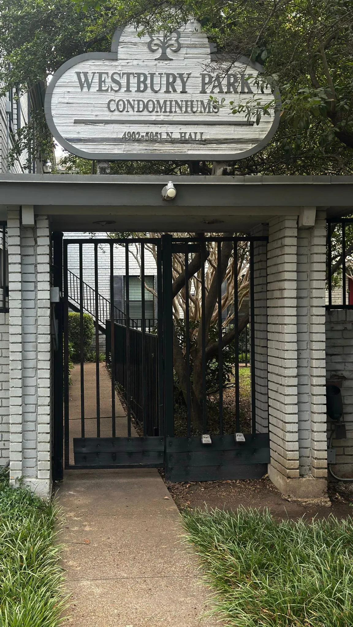 Entry gate featuring a wrought iron design, light-colored brick columns, and a prominent Westbury Park Condominiums sign
