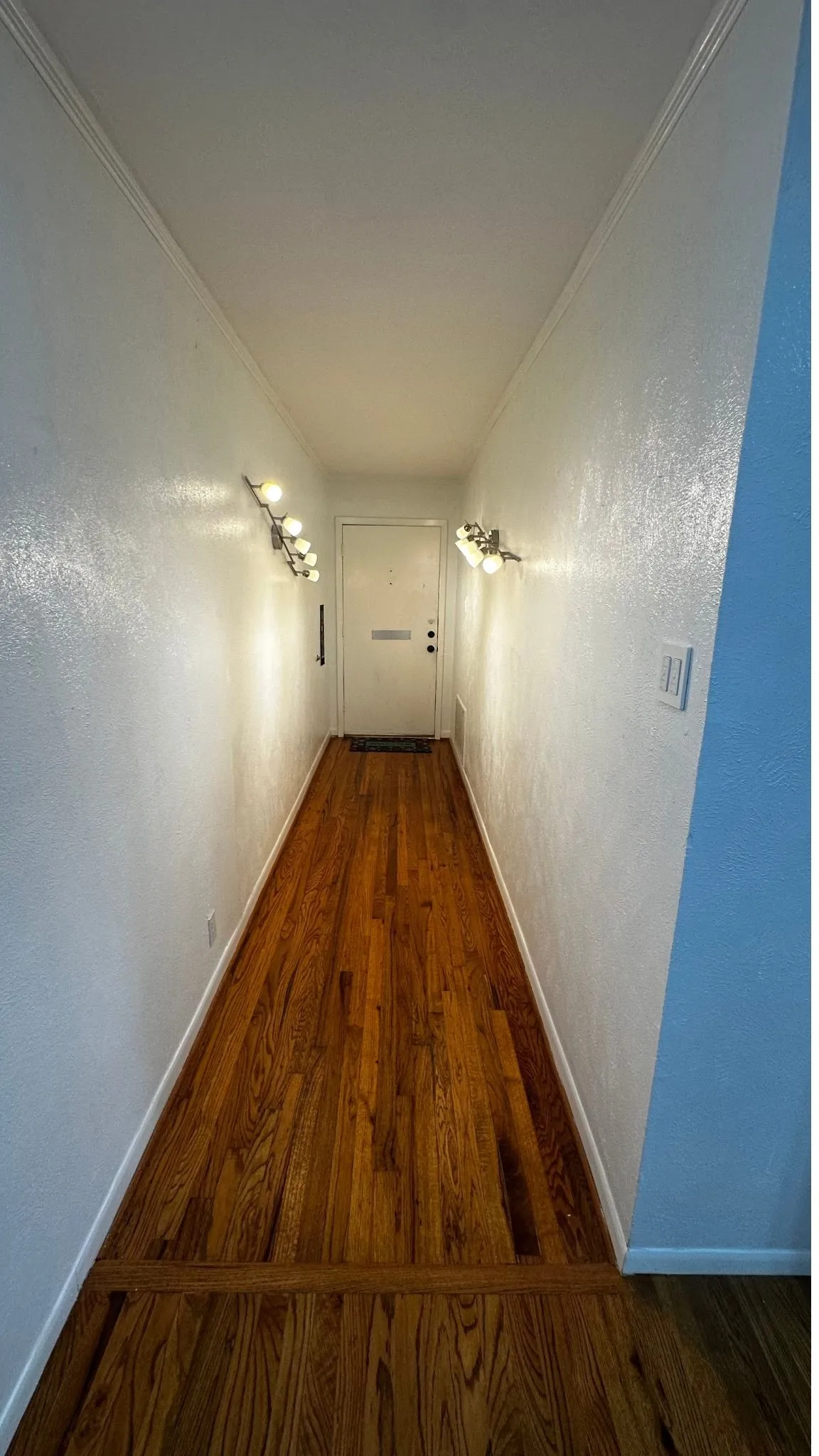 Hardwood flooring extends through the entry hallway, illuminated by two wall-mounted sconces