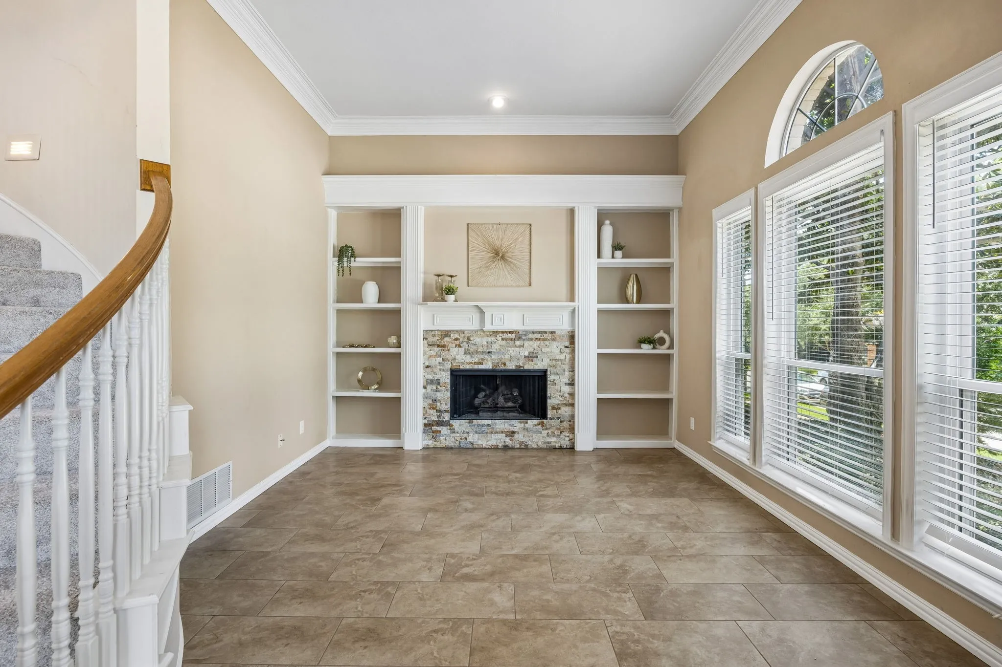 The living room is open to the entry and offers a stacked stone fireplace with gas logs and built in shelving that can create a library or showcase keepsakes. The room has oversized tile flooring and heavy crown moulding.