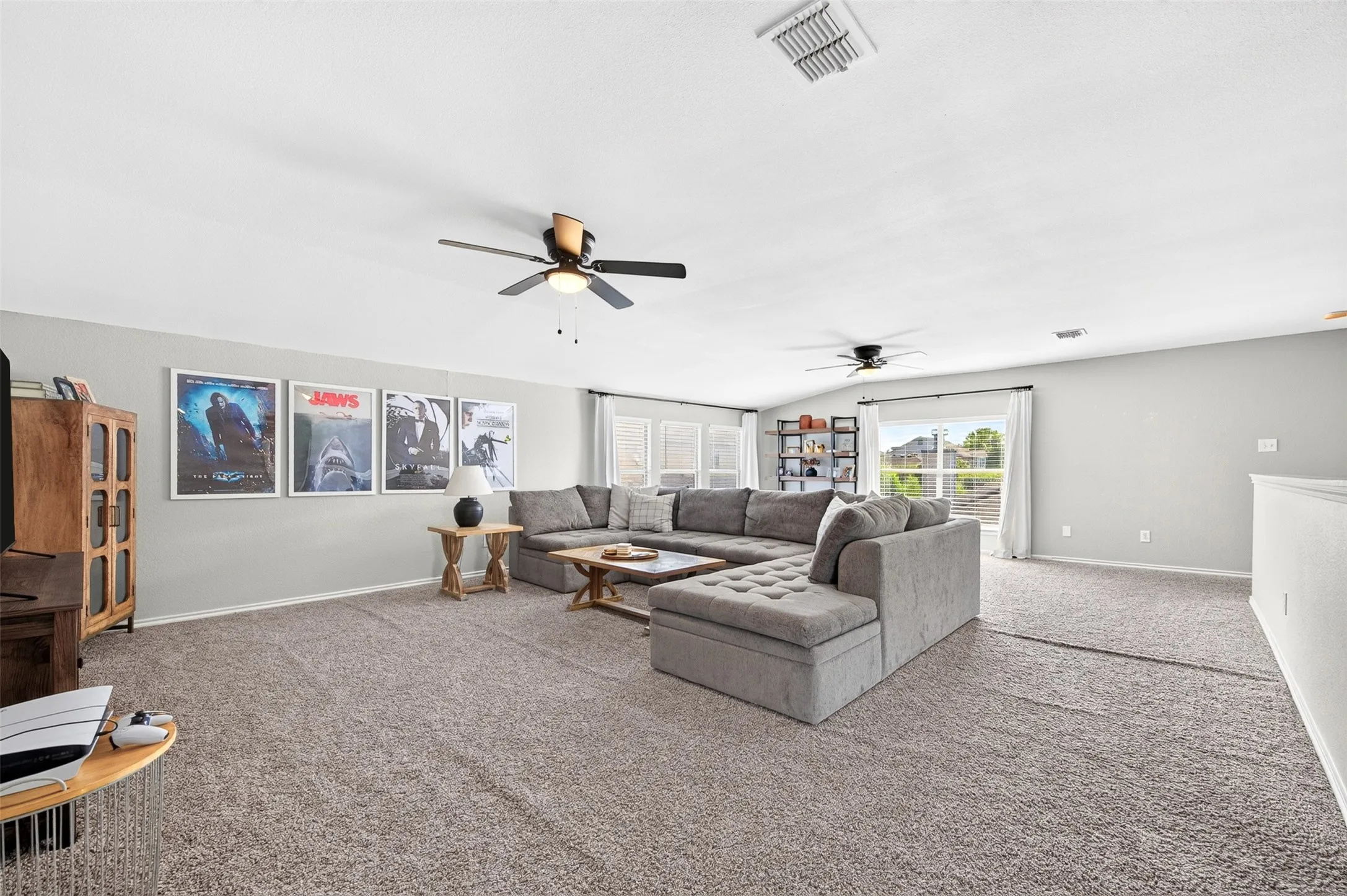 Spacious carpeted room featuring multiple windows, light gray walls, and two ceiling fans with integrated lighting