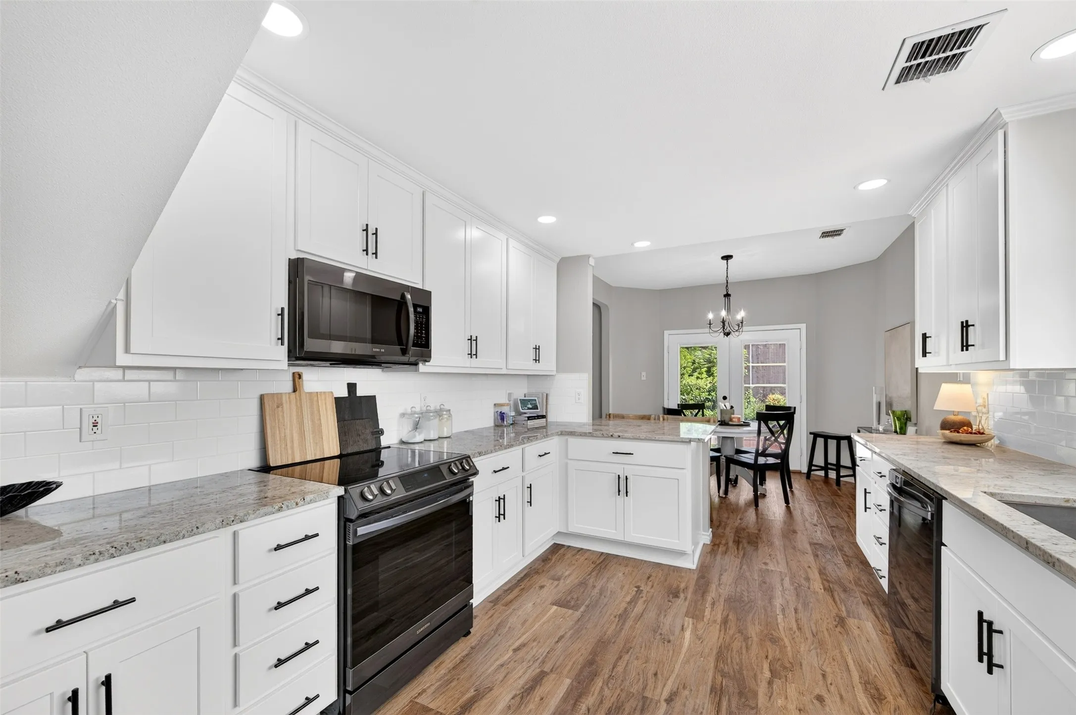 Kitchen featuring white shaker cabinetry, speckled countertops, black appliances, and wood-finish flooring