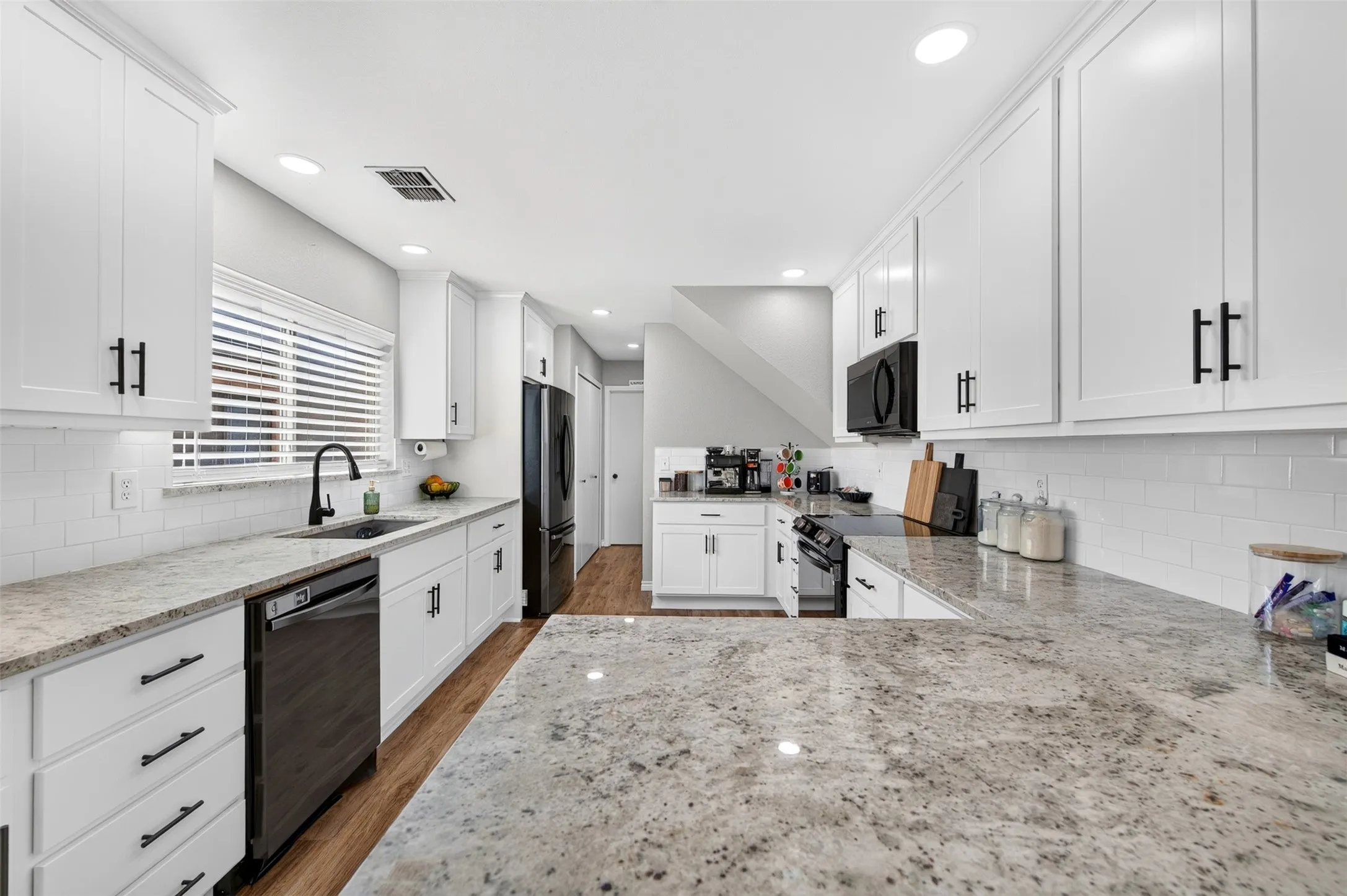 Well-appointed kitchen featuring granite countertops, white shaker cabinetry with matte black hardware, subway tile backsplash, and wood-finish flooring